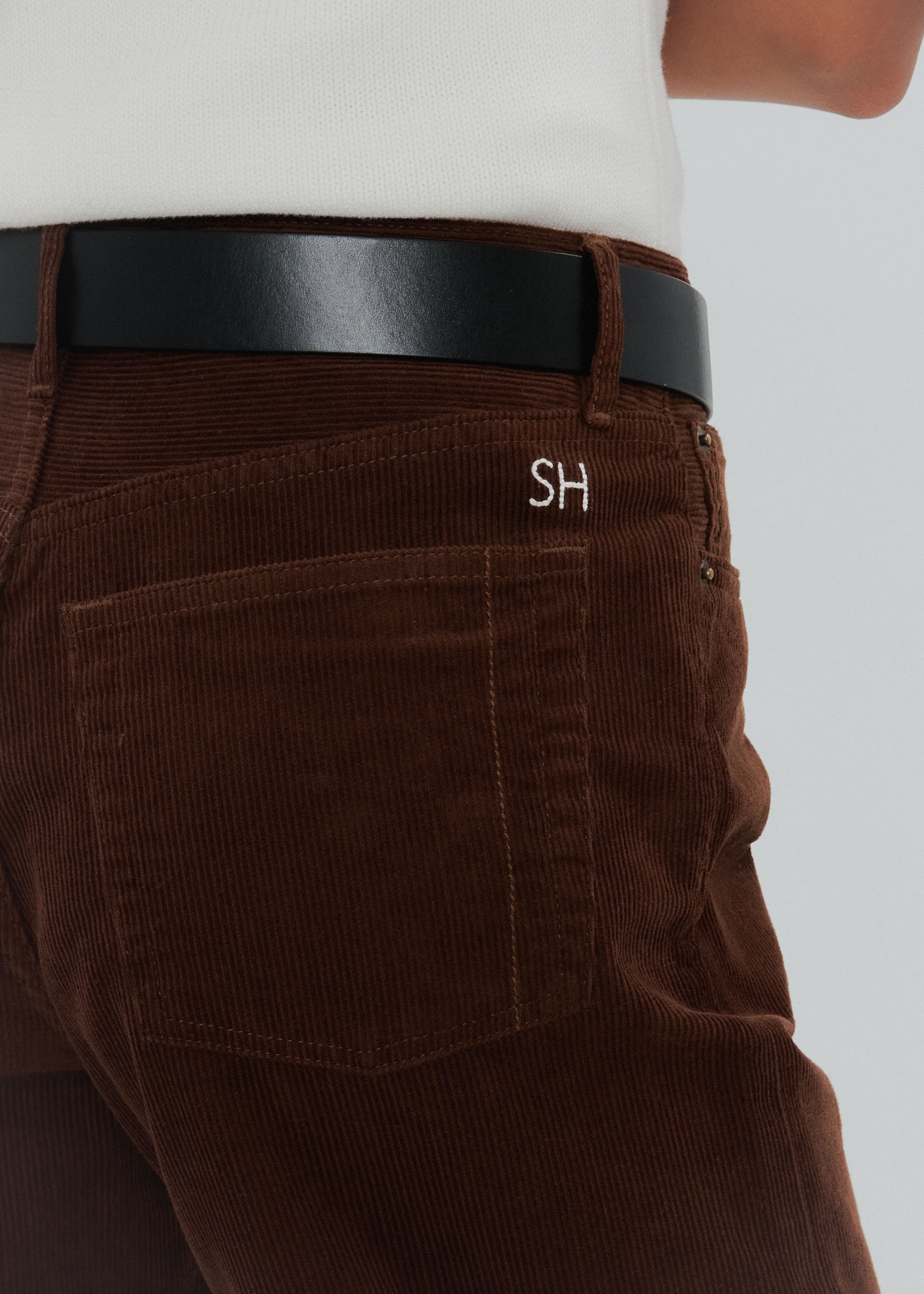 Brown corduroy pants with a black belt and 'SH' logo on a white background
