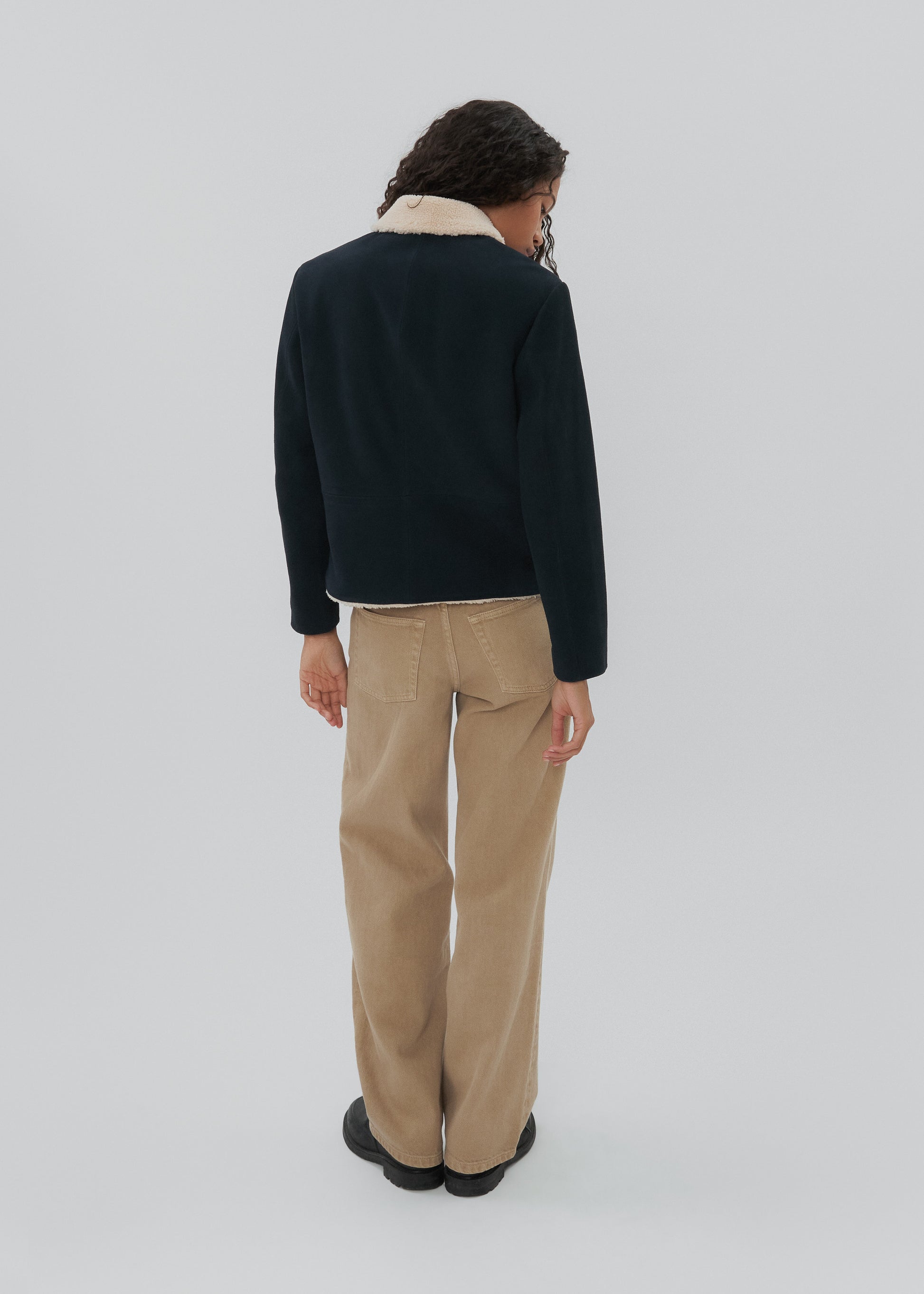 Person wearing a black jacket and beige pants on a white background