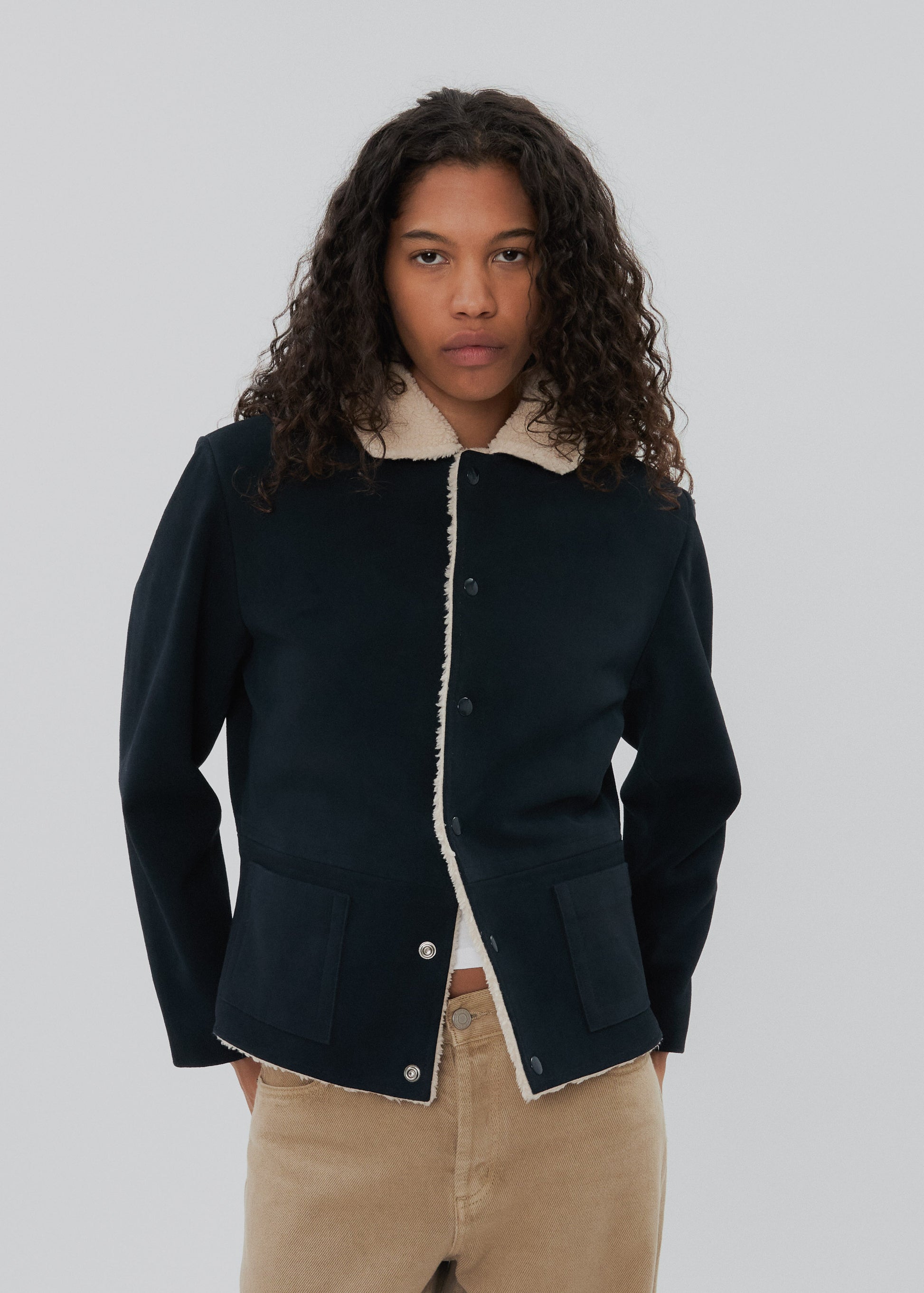 Person wearing a dark blue jacket with white collar and buttons on a plain background