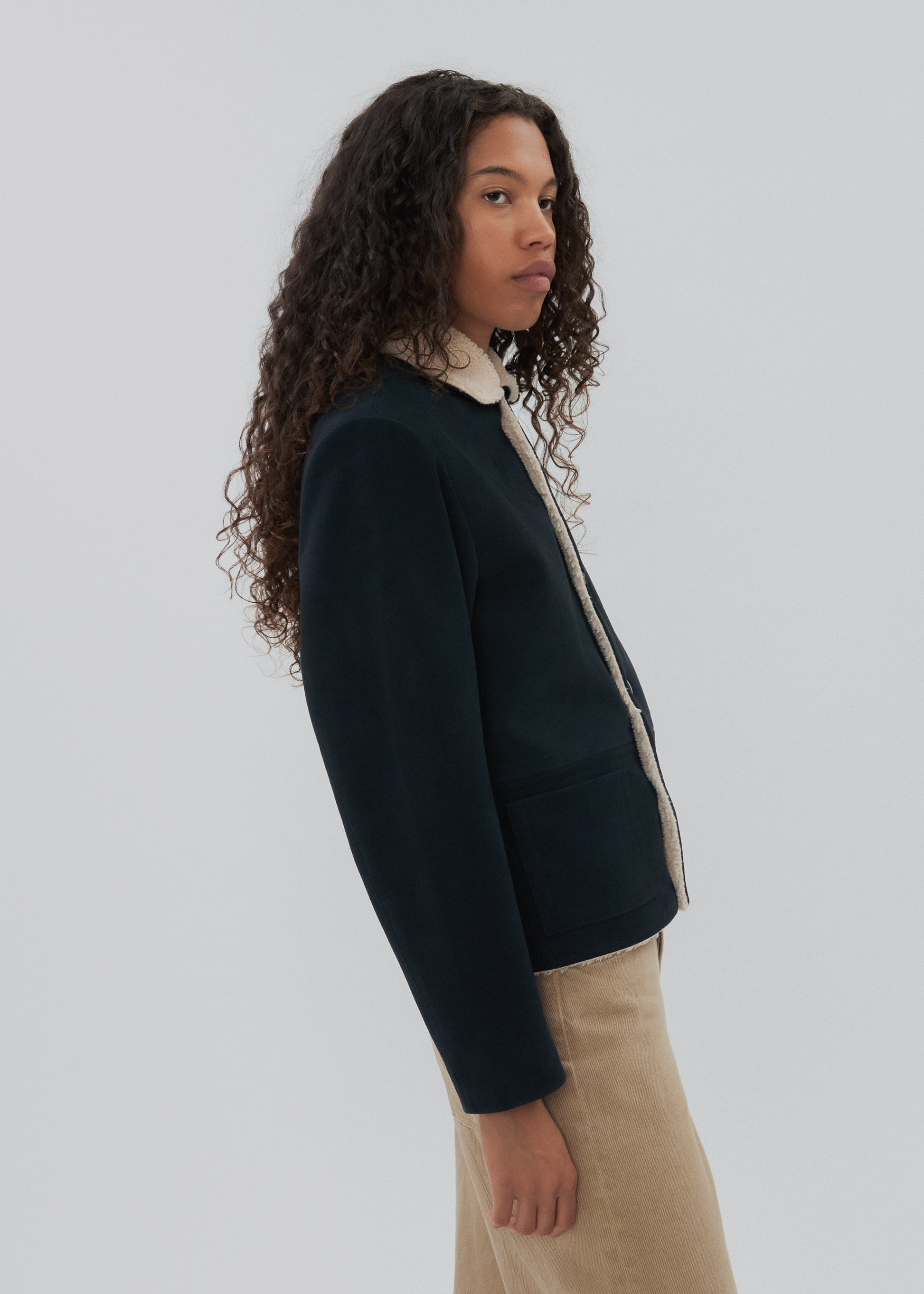 Person wearing a dark jacket with a light shirt underneath on a plain background