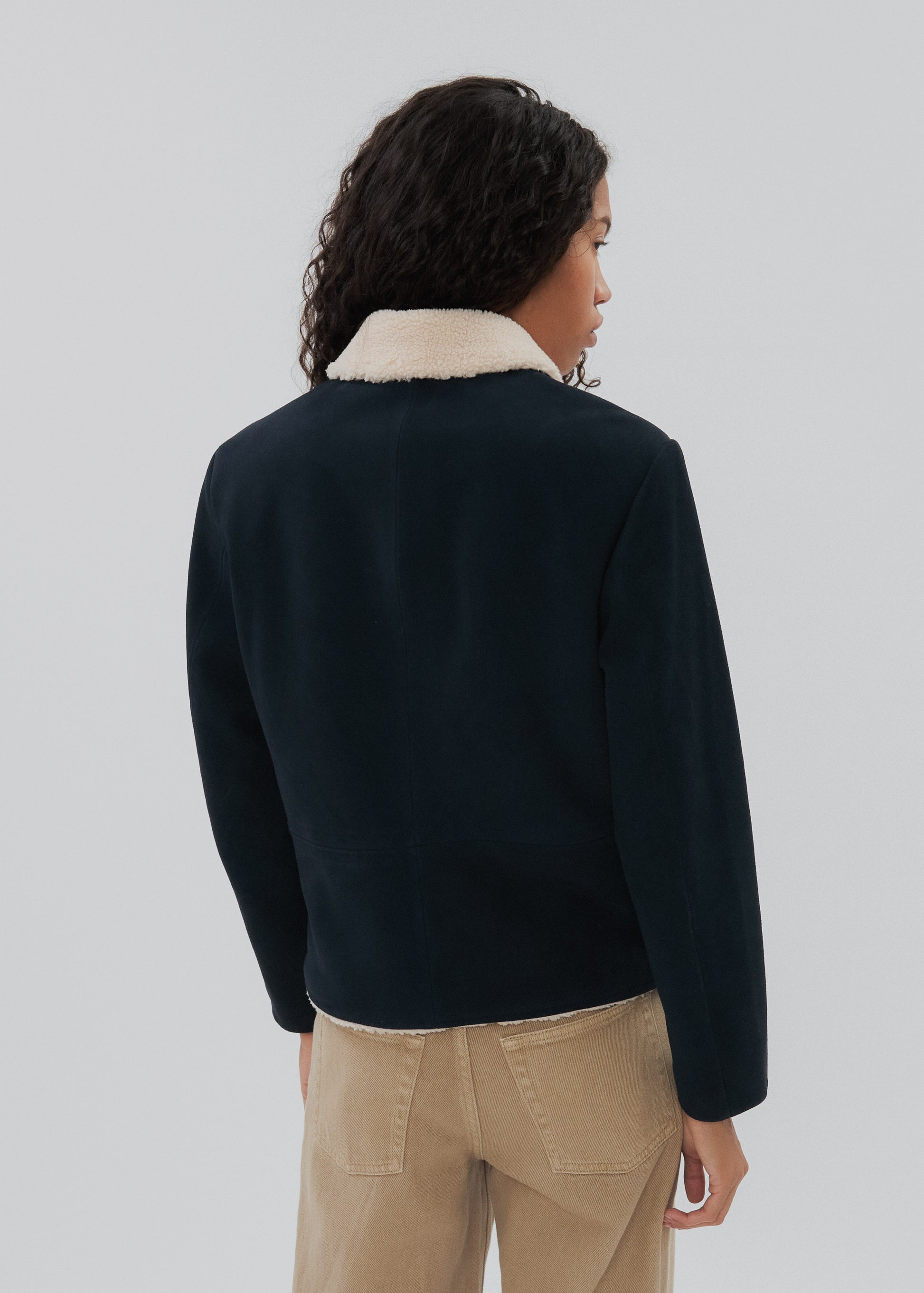 Person wearing a dark jacket with a light-colored collar against a plain background