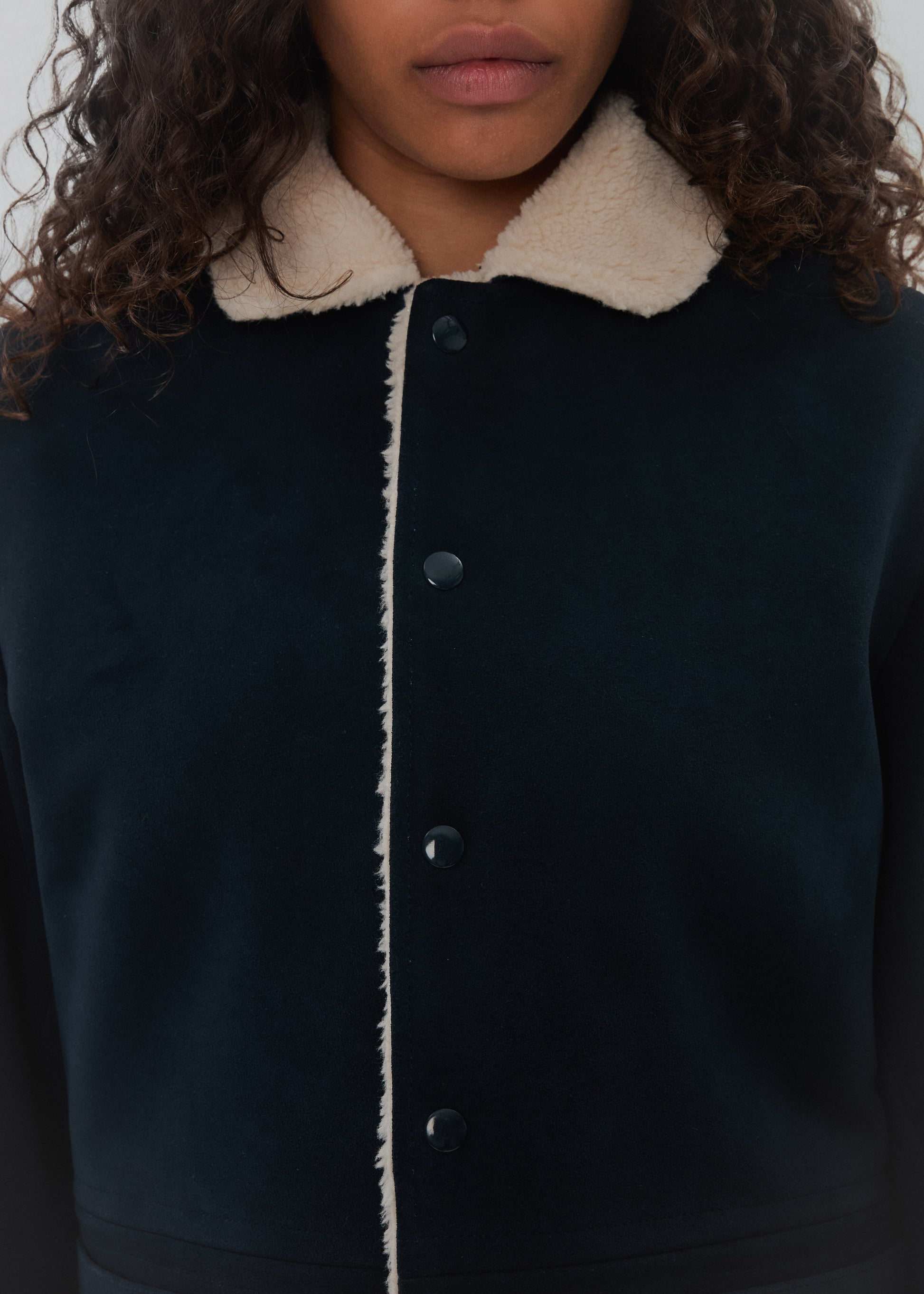 Close-up of a dark coat with a light collar and buttons.