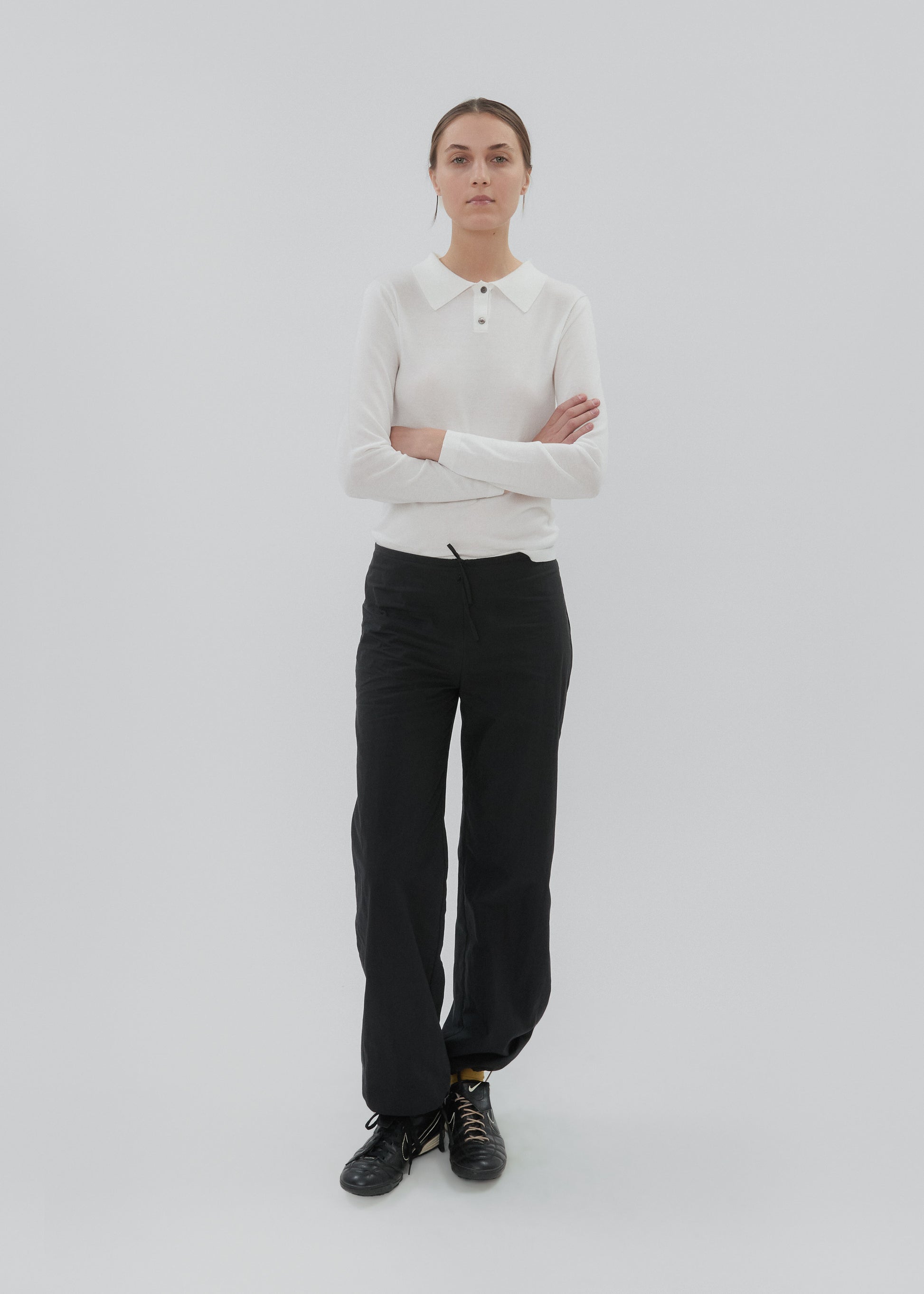 Person wearing a white sweater and black pants on a light gray background
