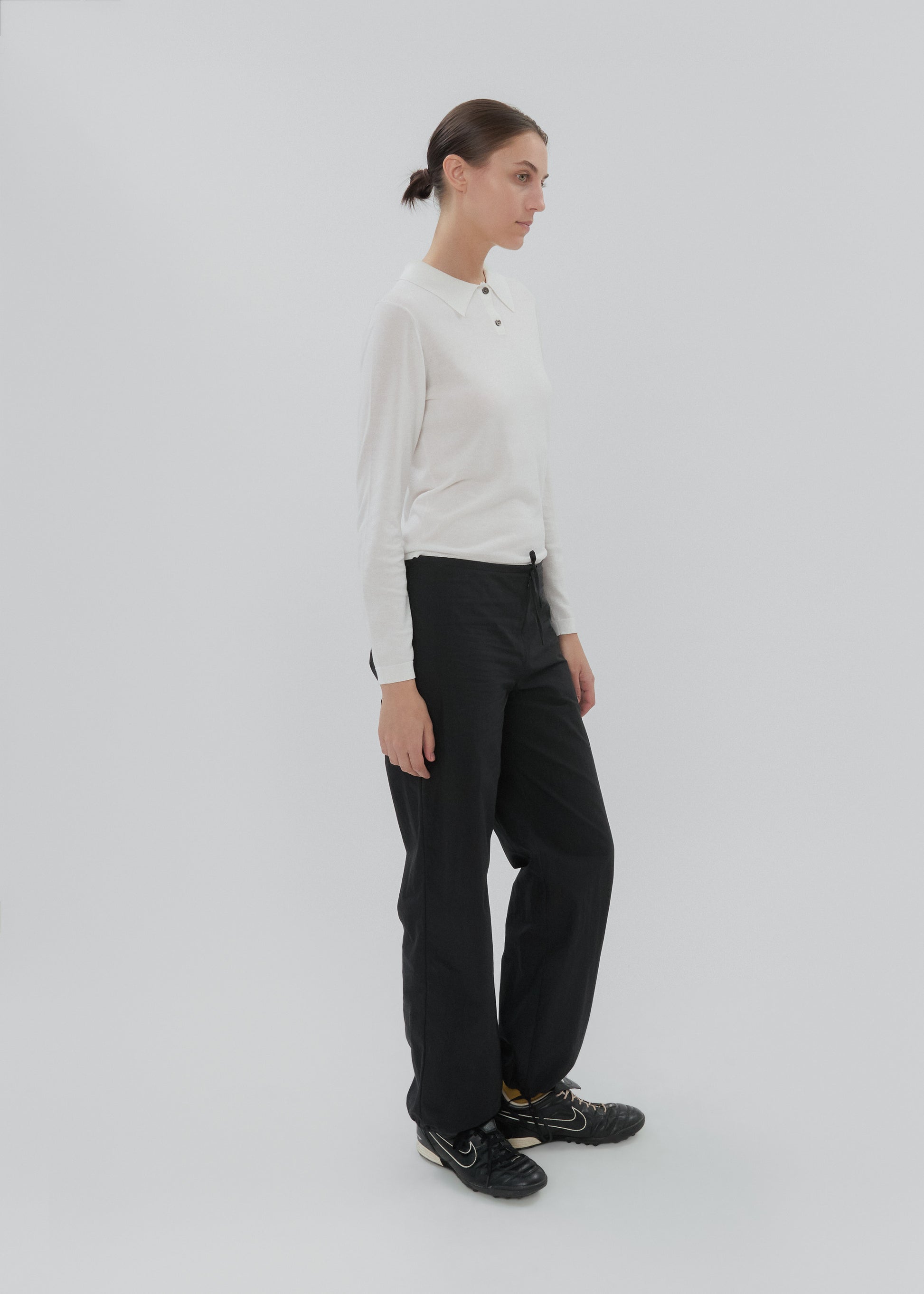 Woman wearing a white long-sleeve shirt and black pants on a light gray background