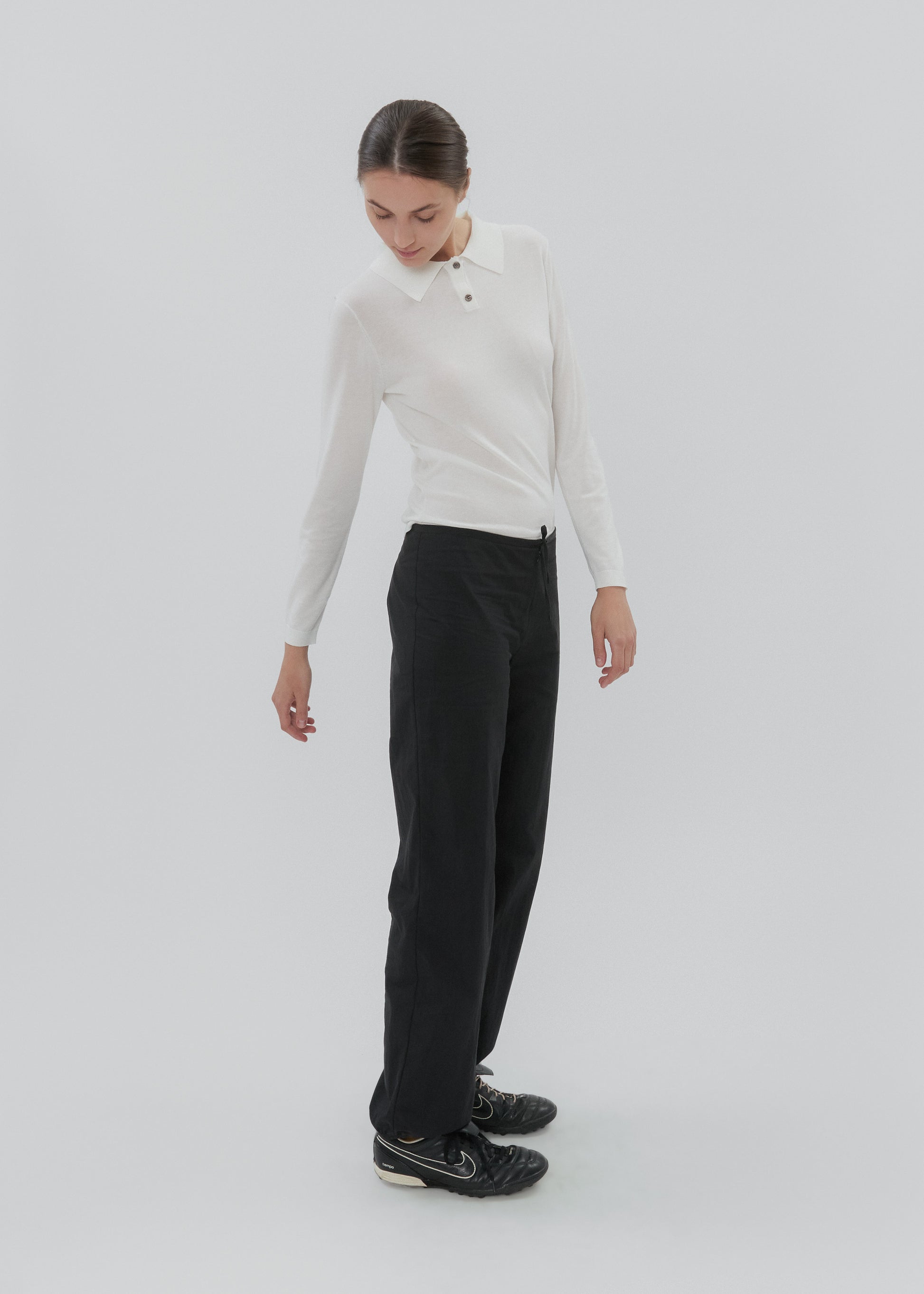 Woman wearing a white long-sleeve top and black pants on a light gray background