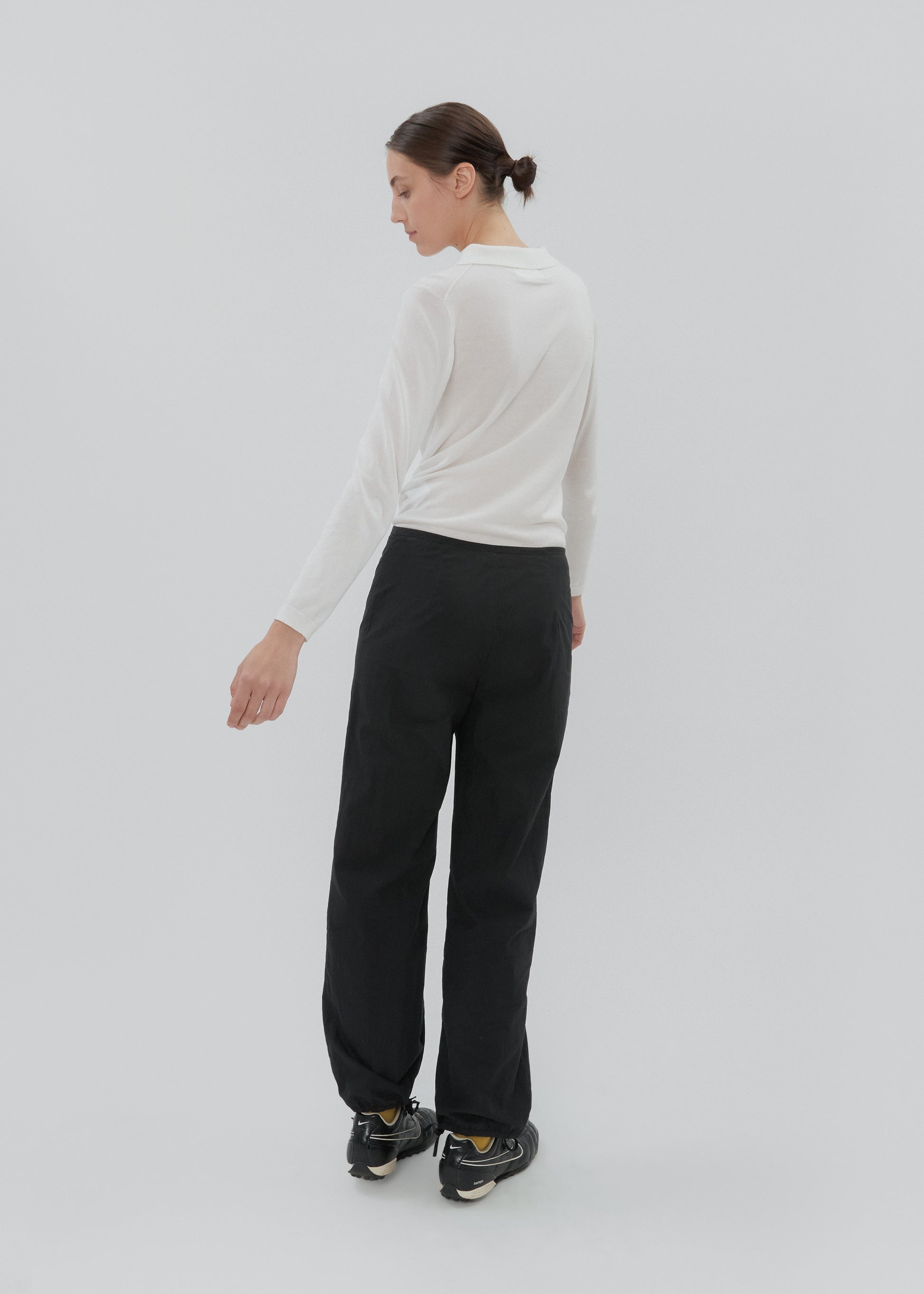 Woman wearing a white long-sleeve top and black pants on a light gray background