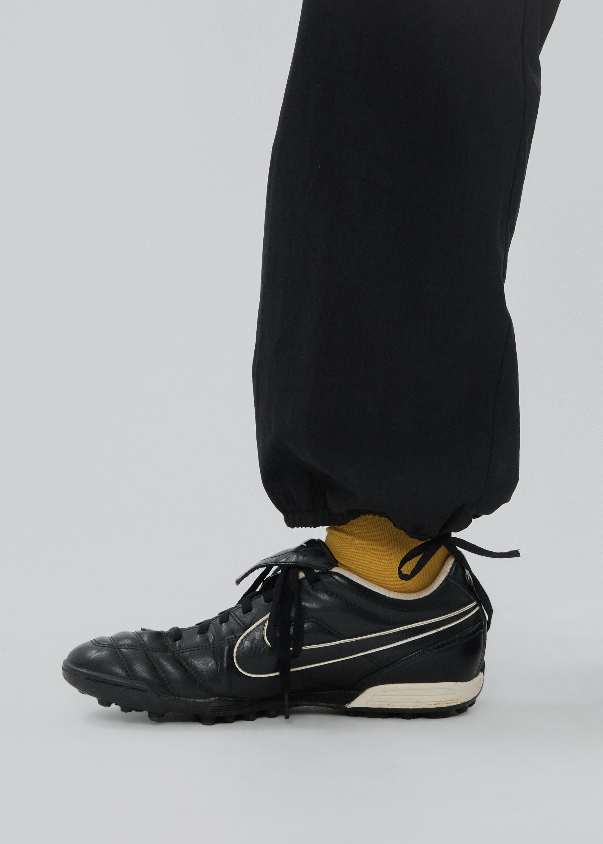Black soccer cleats with a Nike logo worn with black pants on a light gray background