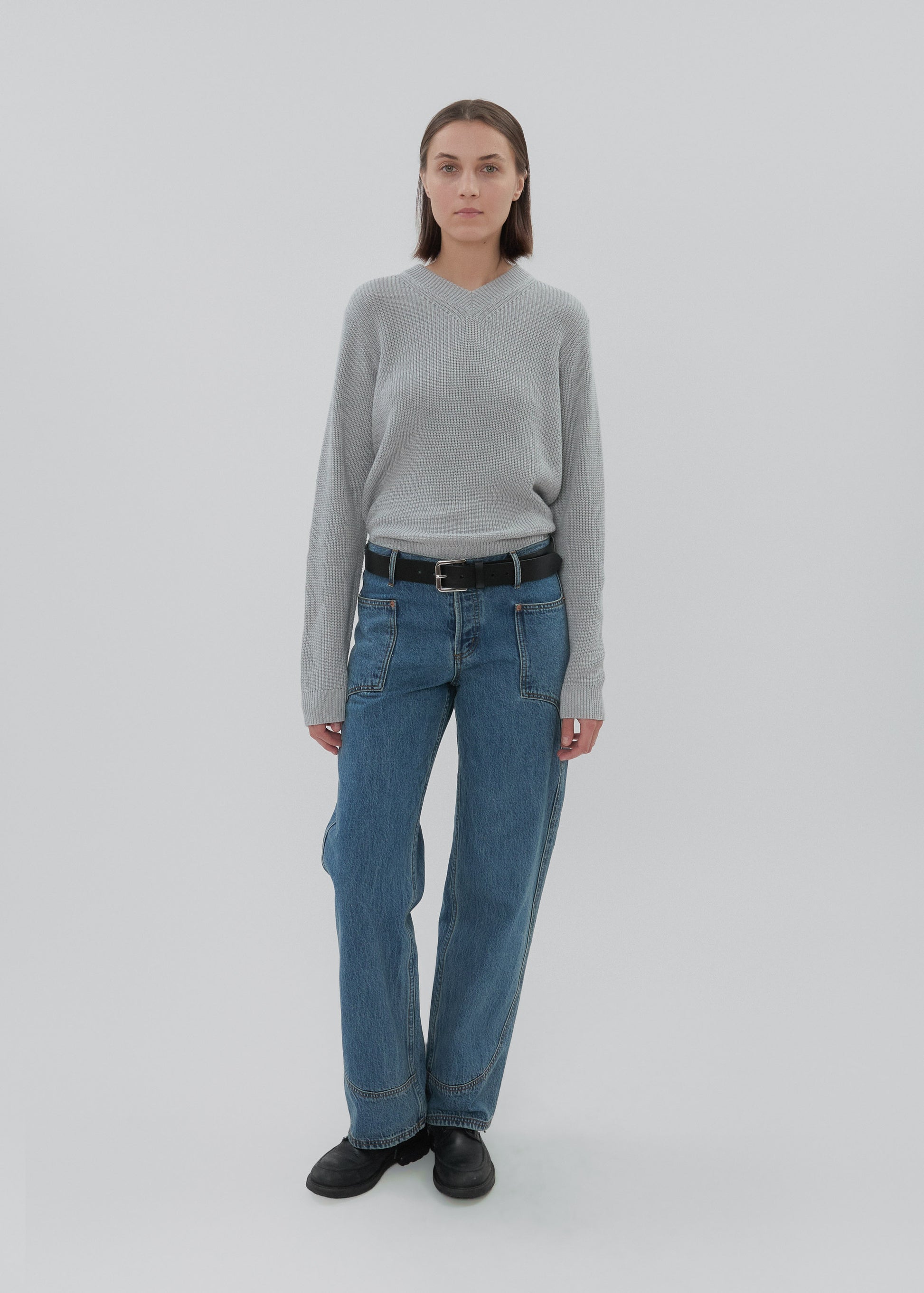Person wearing a gray sweater and blue jeans on a white background