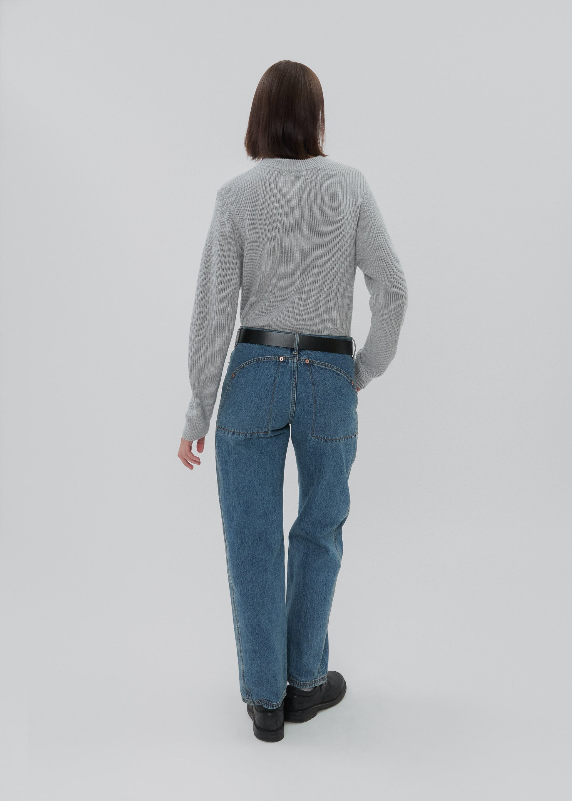 Person wearing a gray sweater and blue jeans on a white background