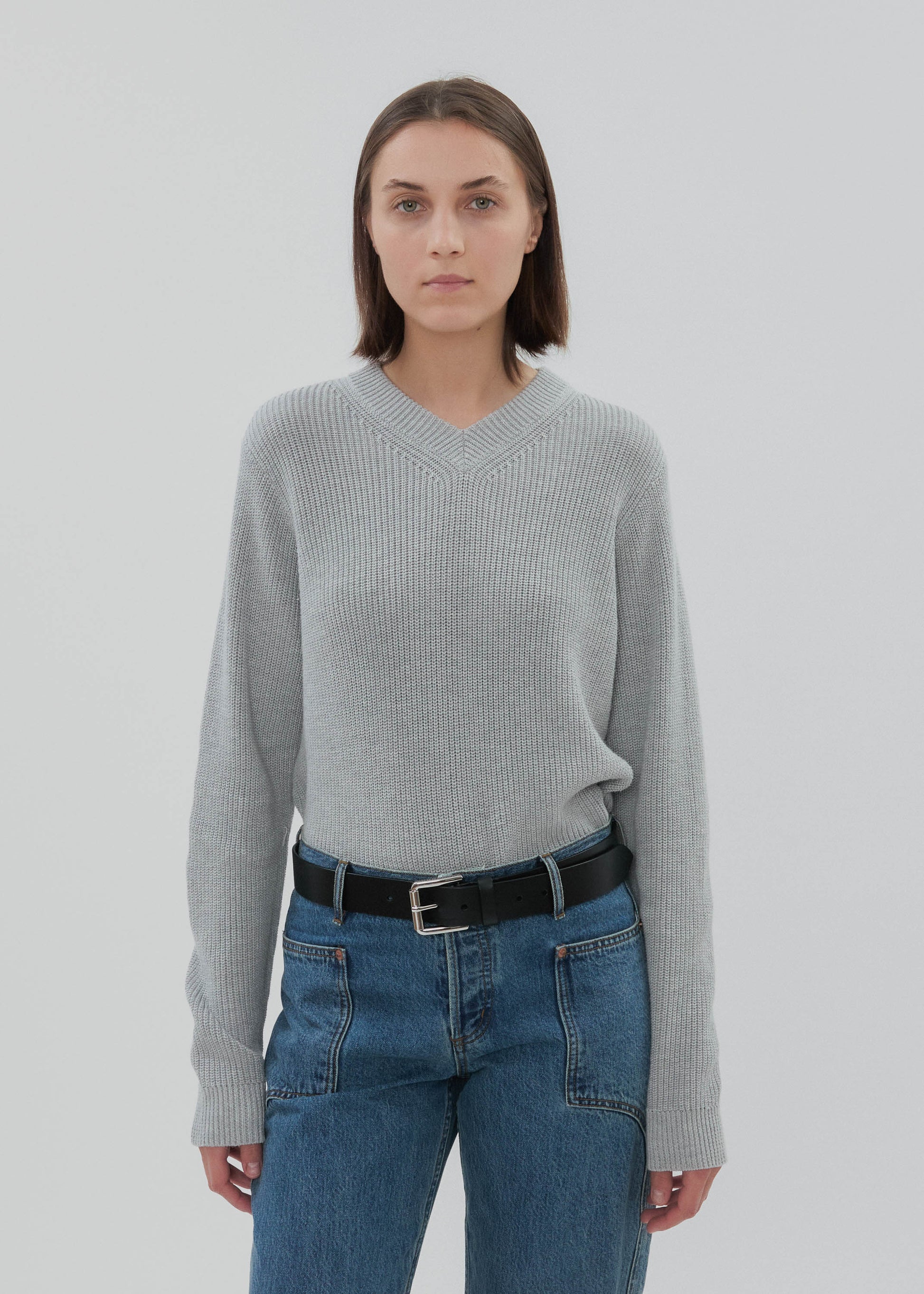 Person wearing a gray sweater and blue jeans on a white background