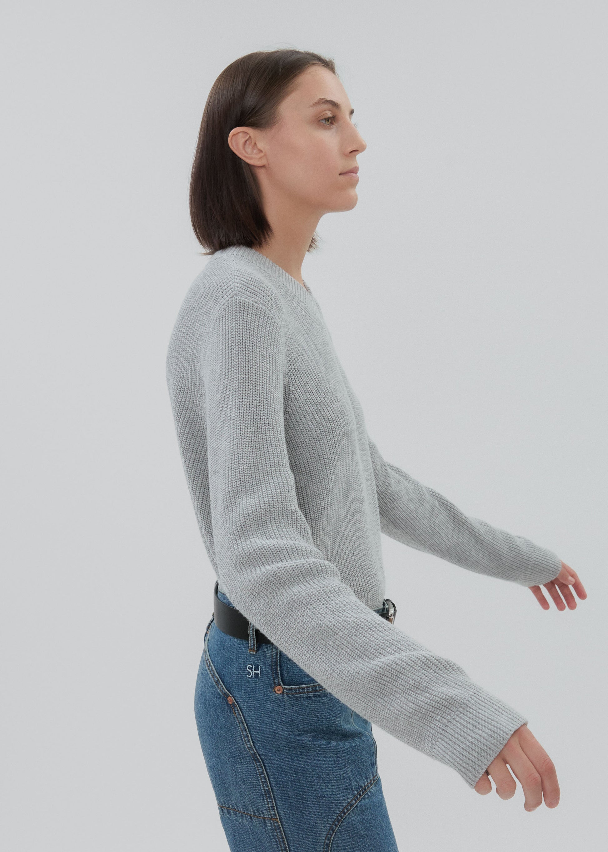 Woman wearing a gray sweater and blue jeans on a light gray background