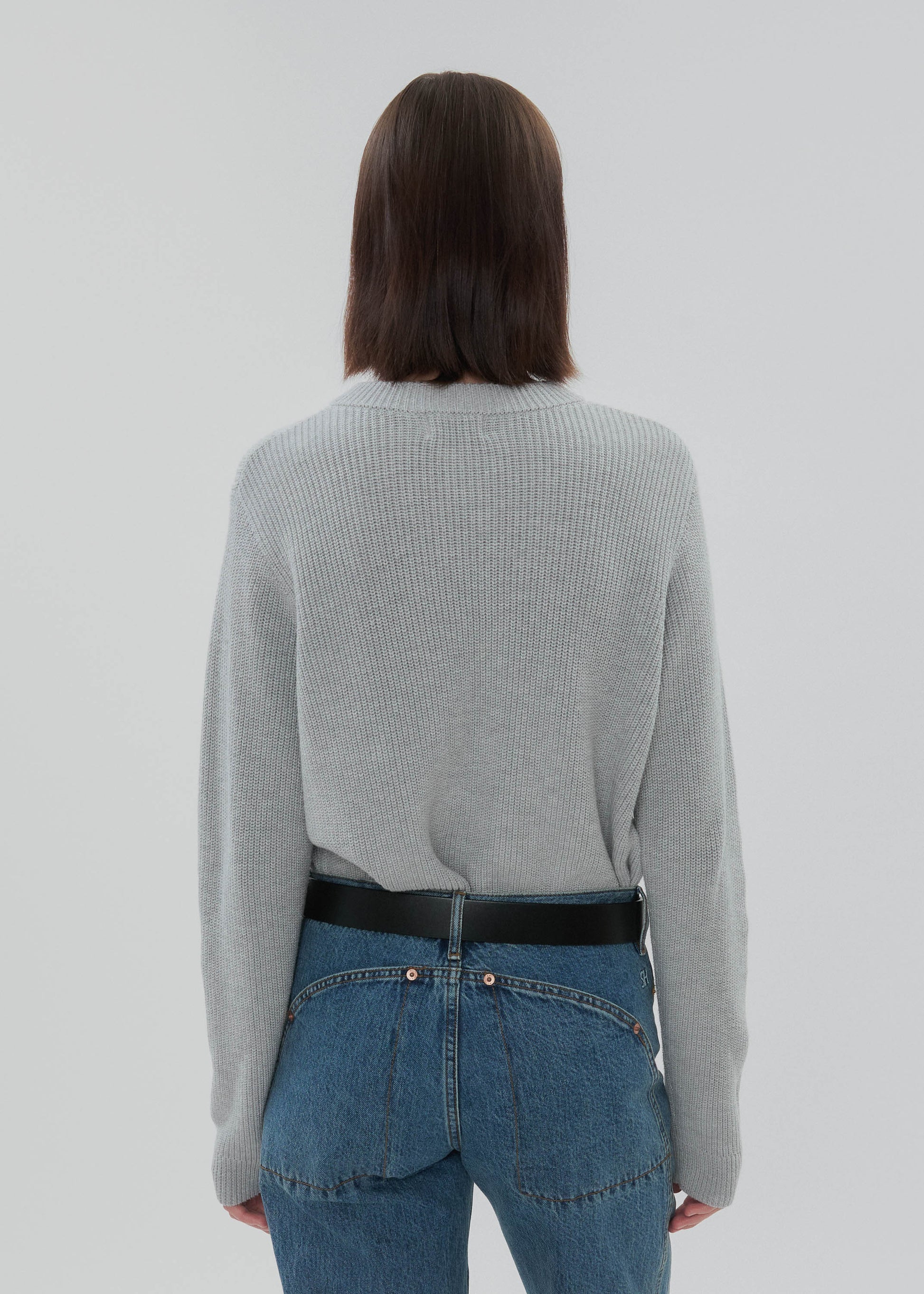Person wearing a gray sweater and blue jeans from behind on a light gray background