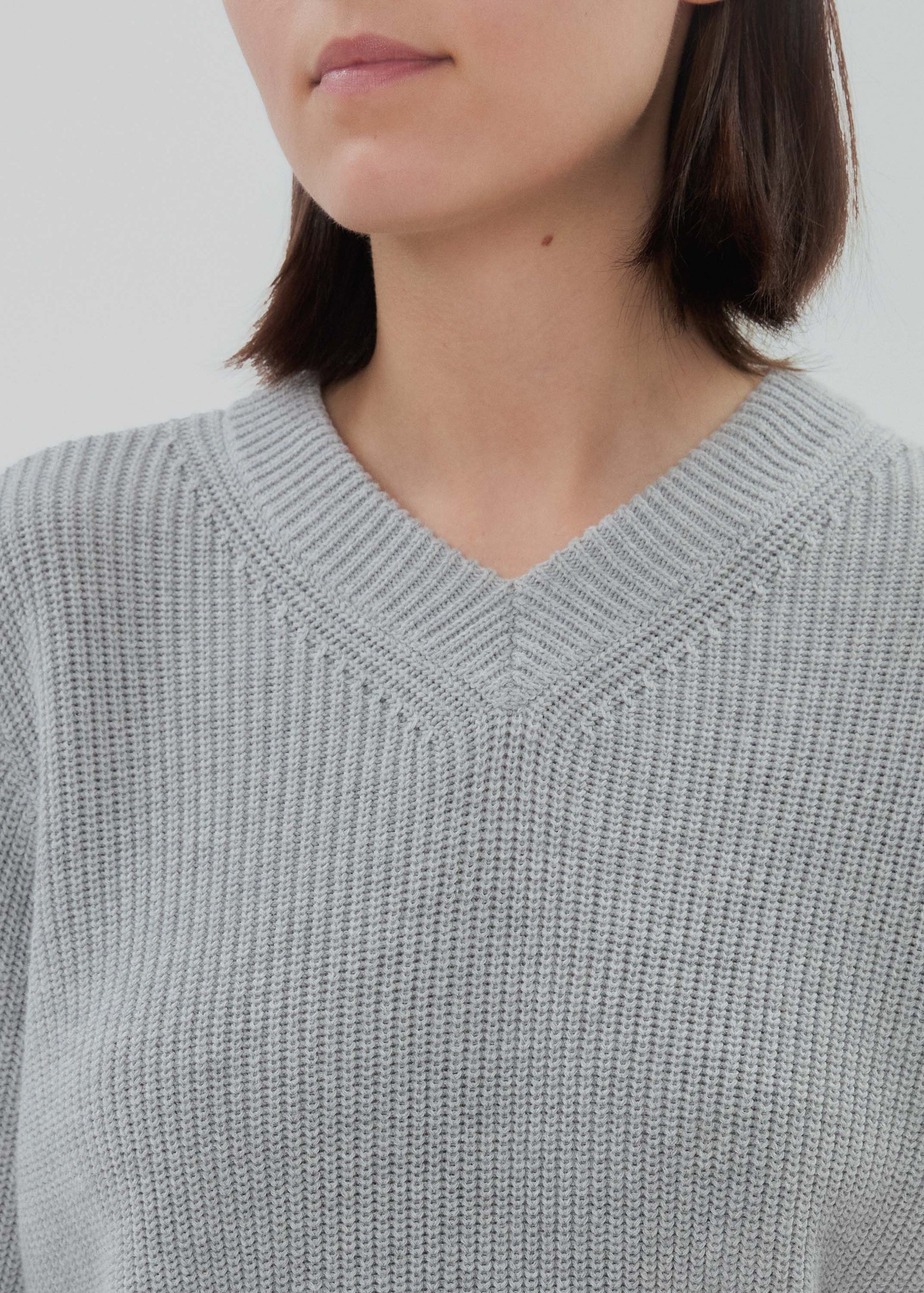 Close-up of a person wearing a light gray sweater with a plain background