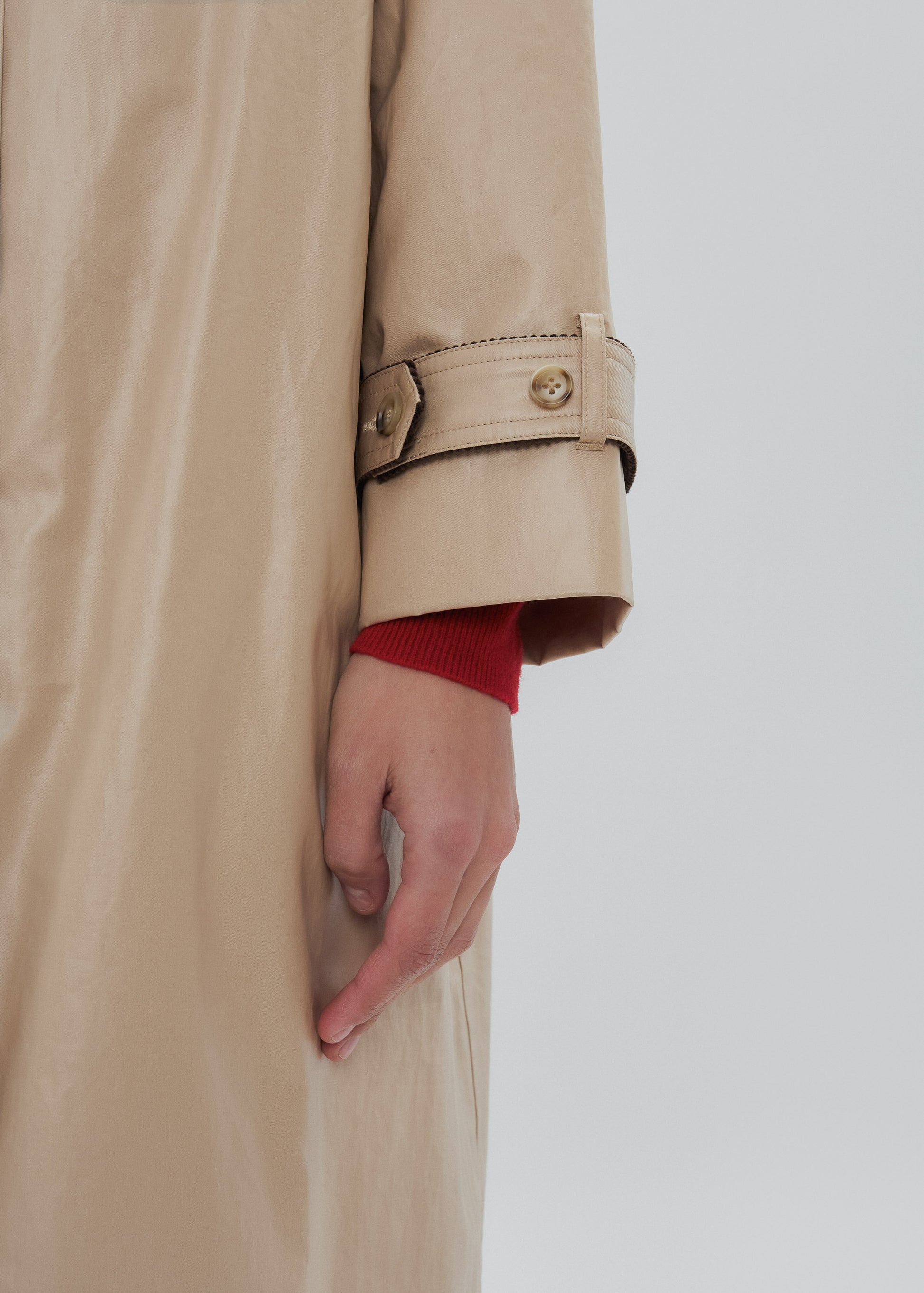 Beige trench coat with a hand peeking out from under the sleeve against a light background