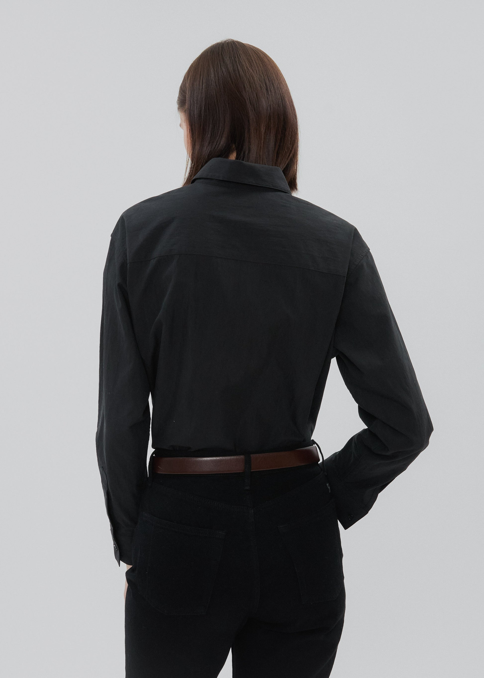 Person wearing a black shirt and dark pants on a light gray background