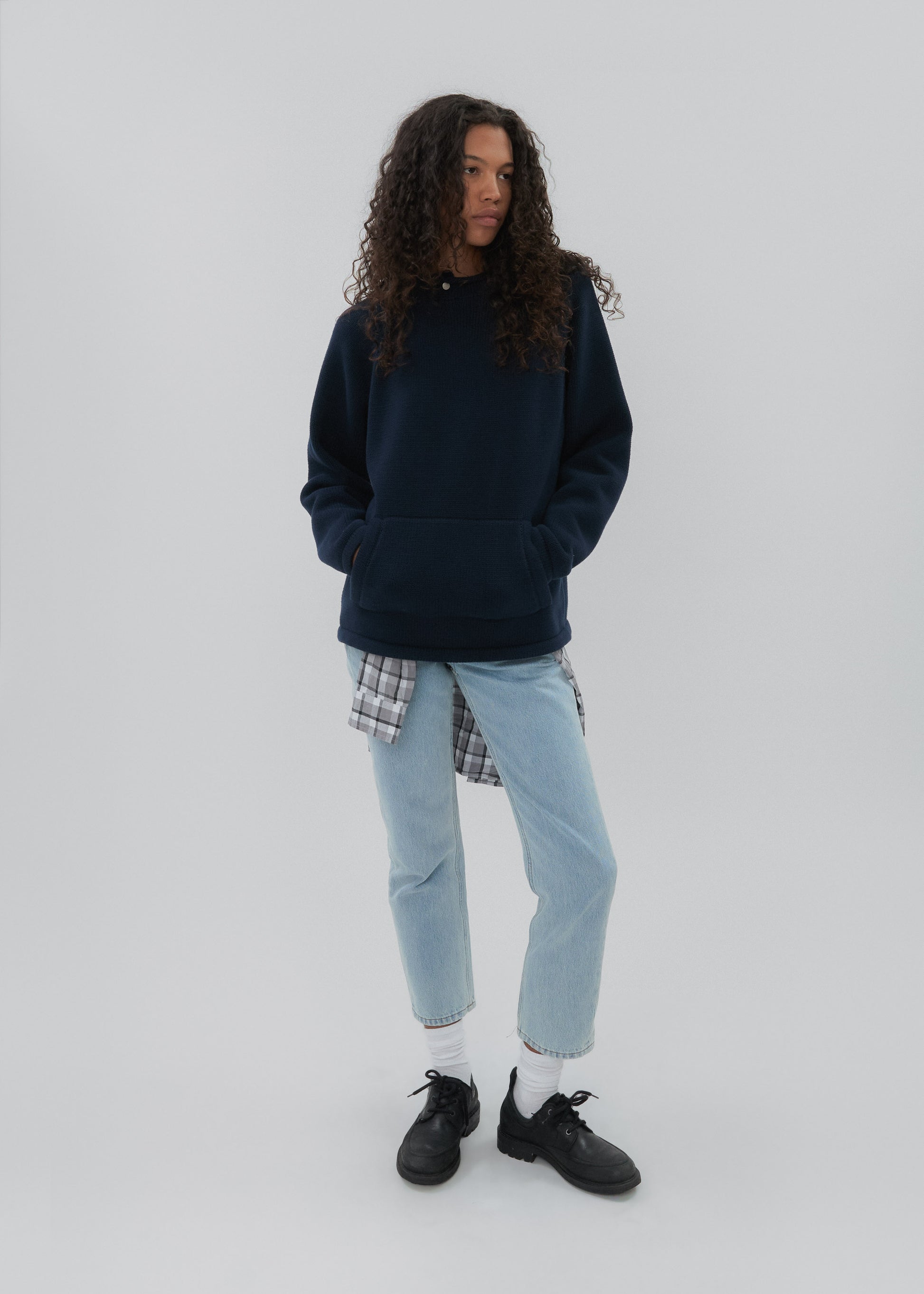 Person wearing a navy hoodie, light blue jeans, and black shoes on a white background