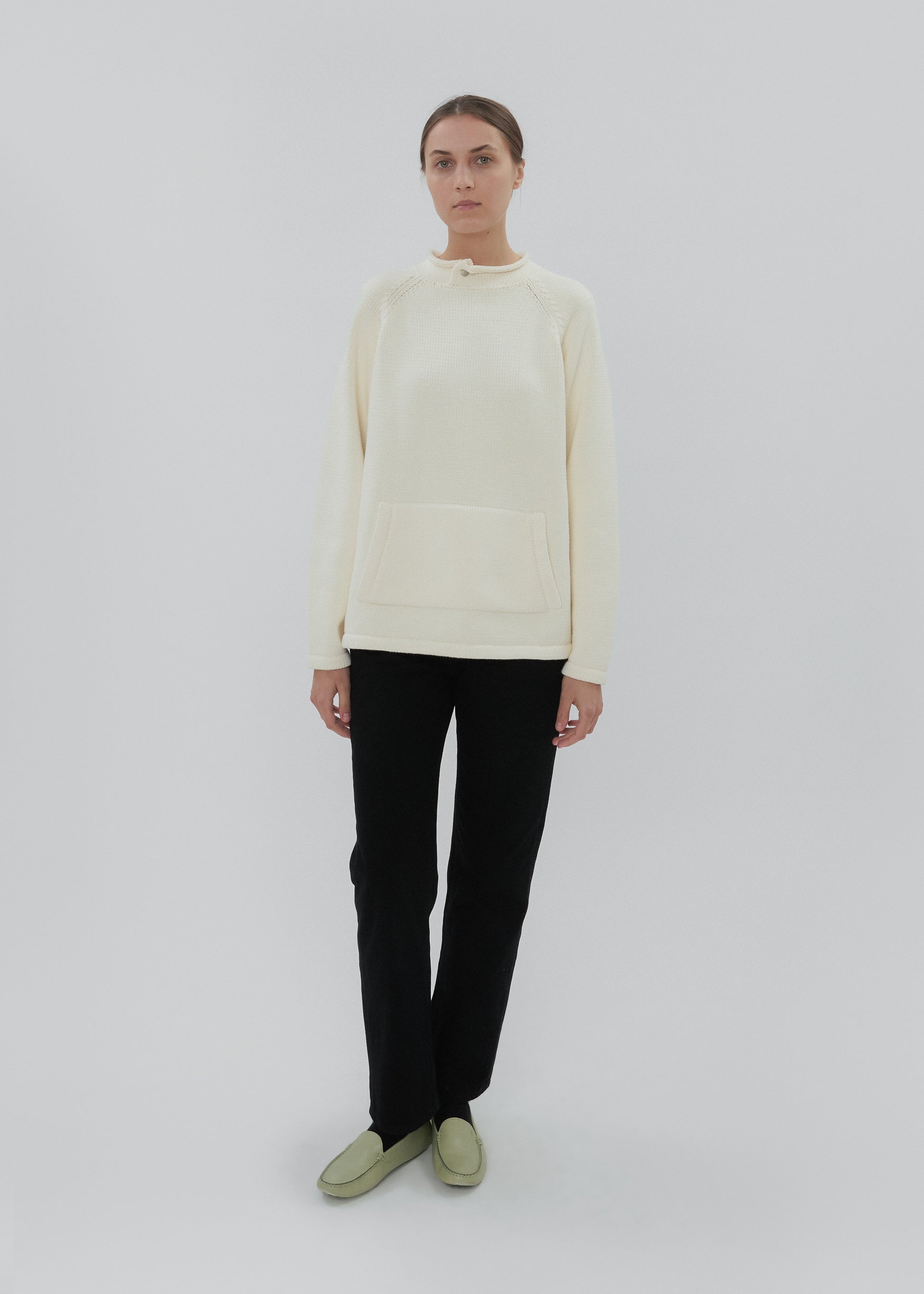 Person wearing a light-colored sweater and black pants on a white background