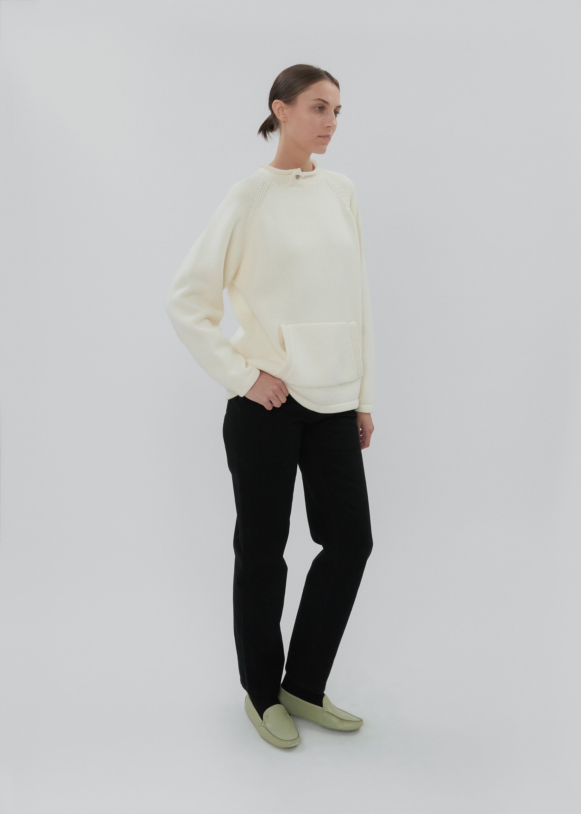 Woman wearing a cream sweater and black pants on a white background