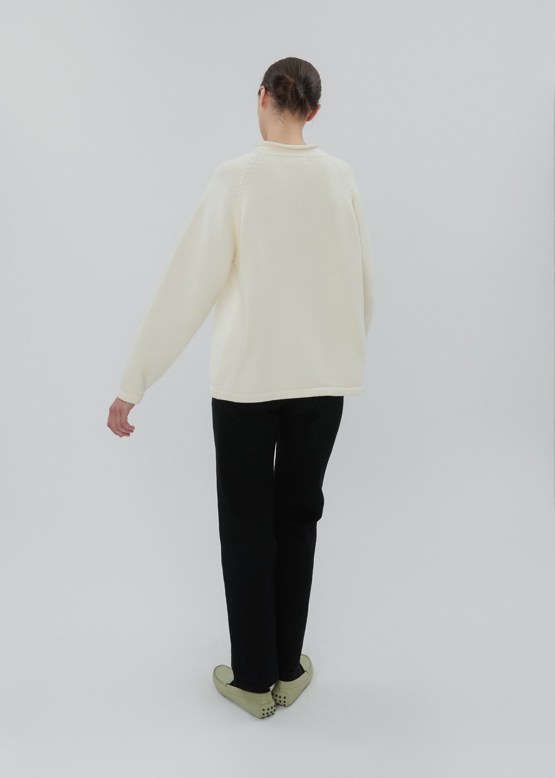 Person wearing a cream sweater and black pants on a white background