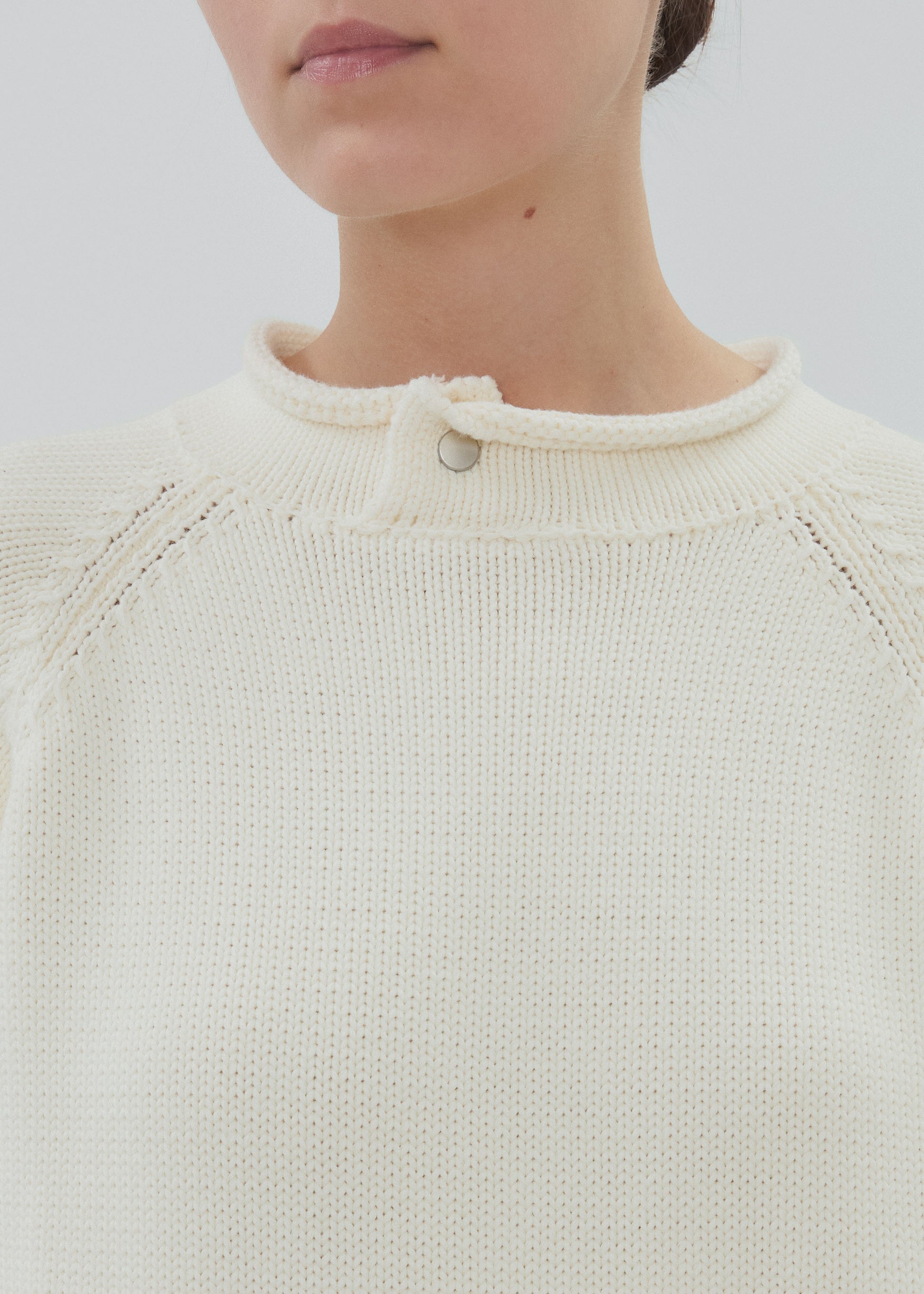 Close-up of a person wearing a cream-colored knit sweater with a plain background
