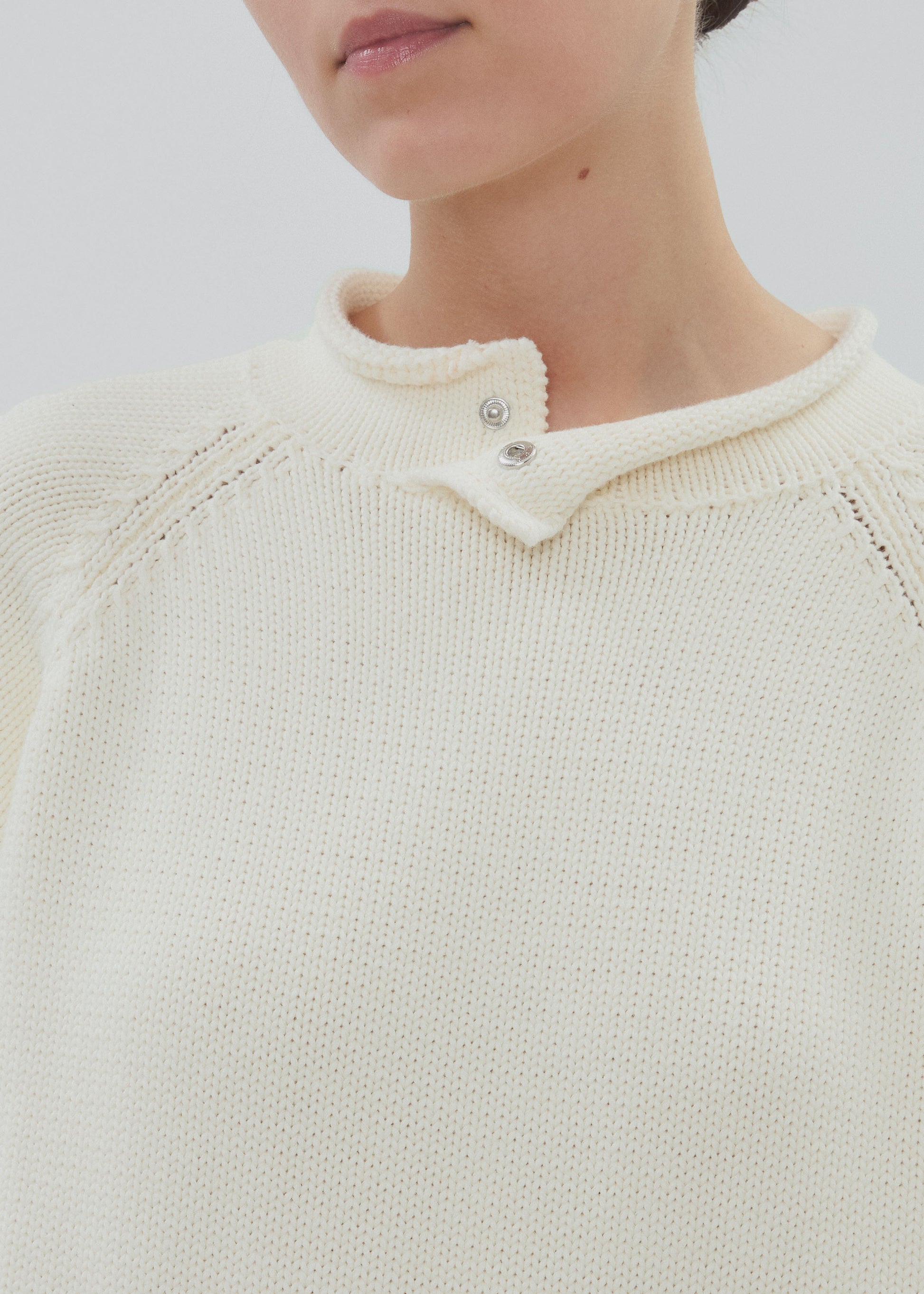 Close-up of a person wearing a cream-colored knit sweater with a textured collar.