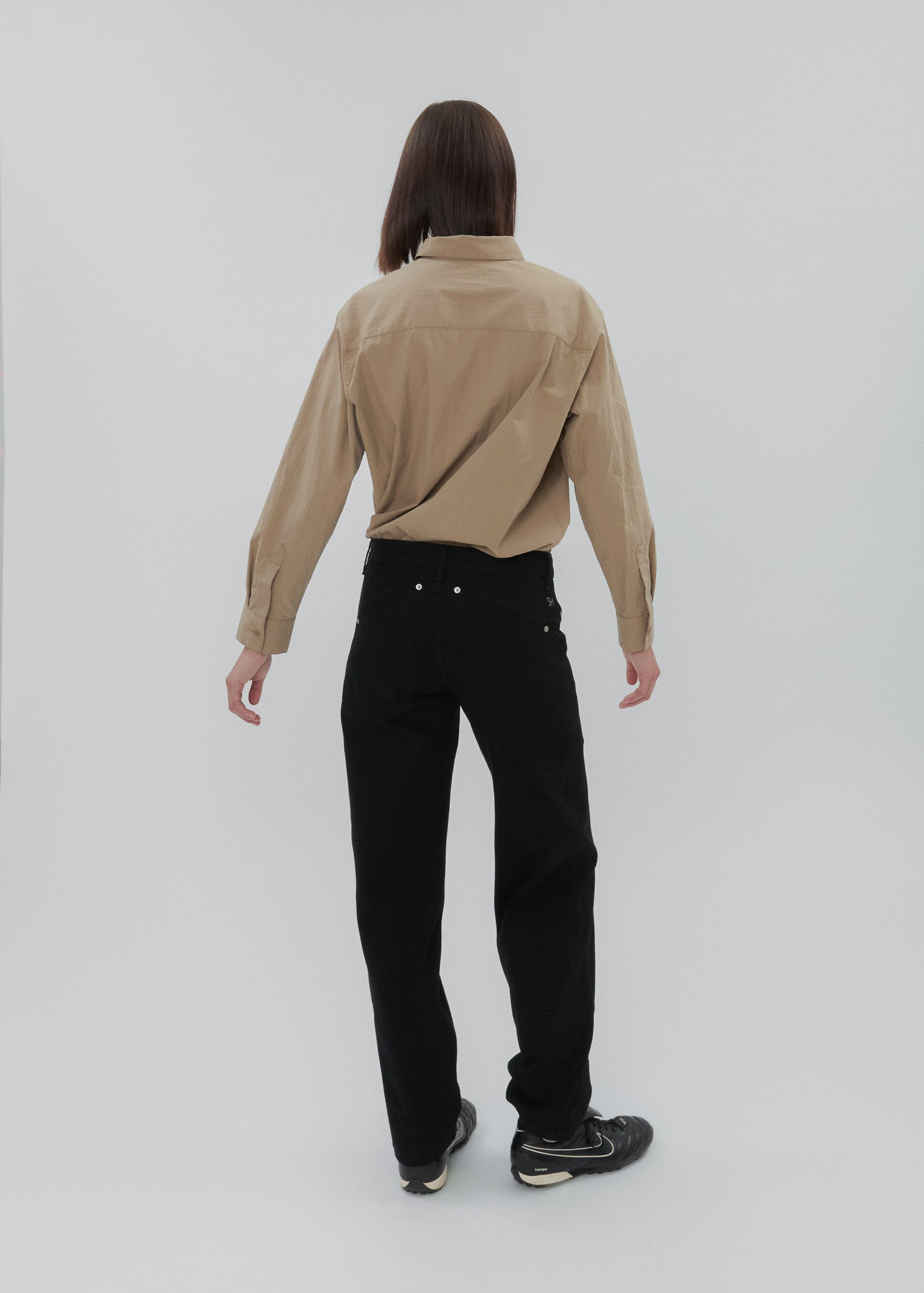 Person wearing a beige shirt and black pants on a white background