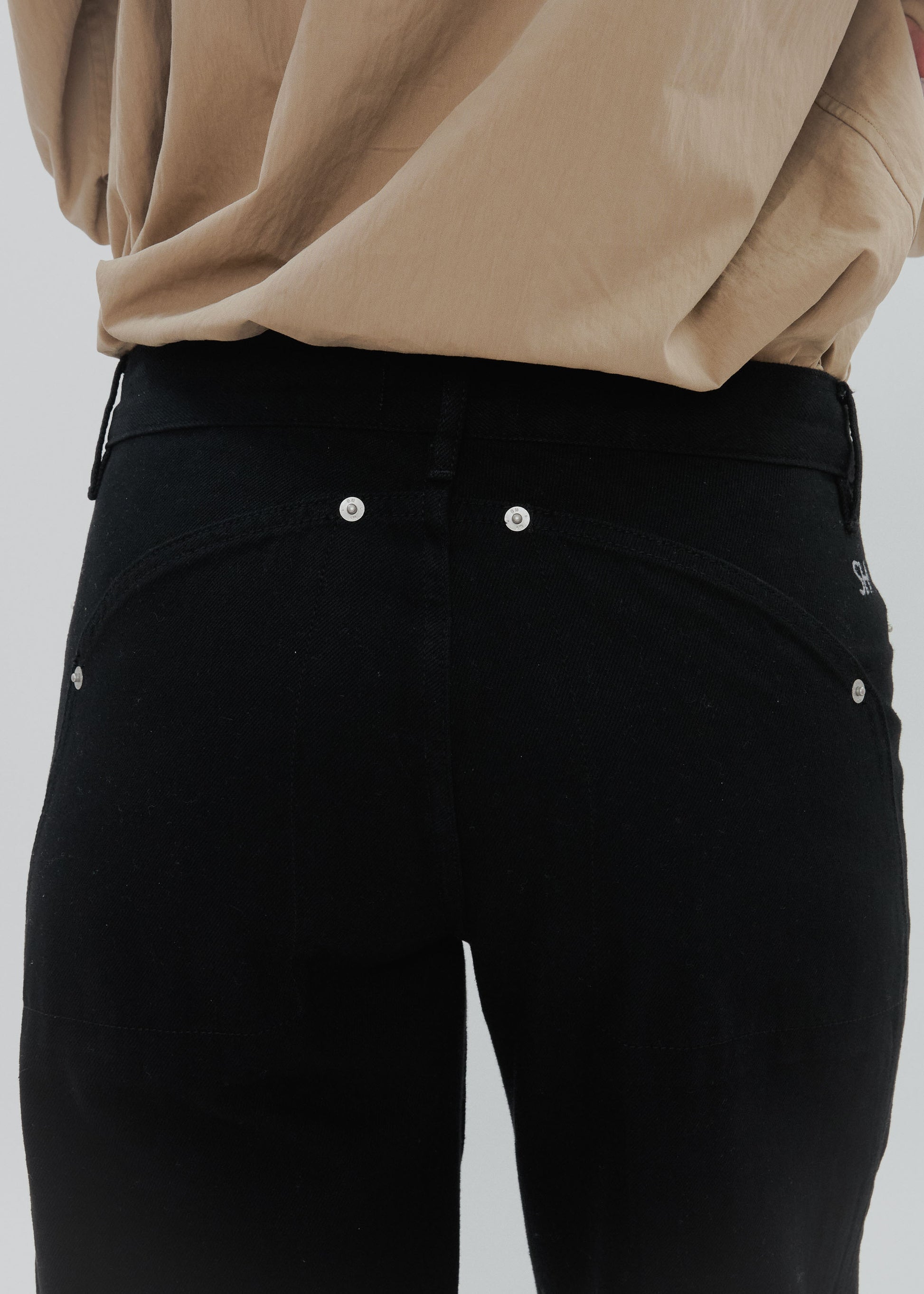 Black pants with silver buttons worn by a person in a beige top on a light gray background