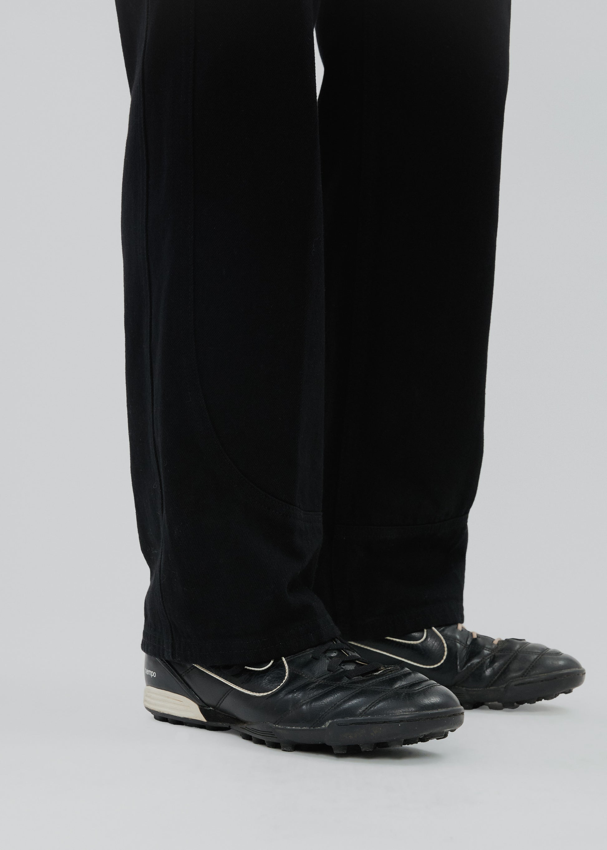 Black soccer cleats worn with black pants on a light gray background