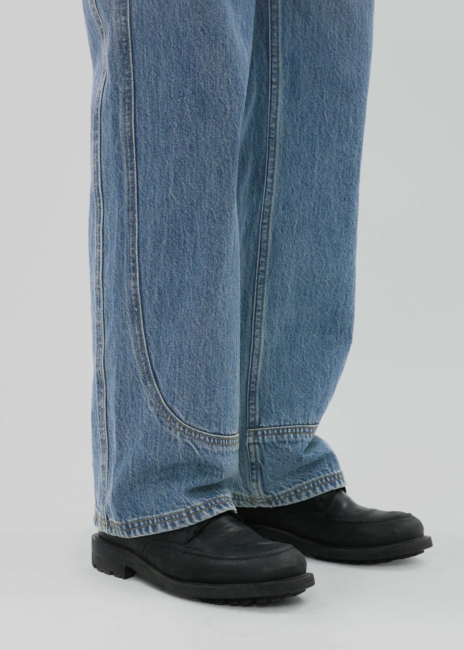 Person wearing blue jeans and black shoes on a light gray background