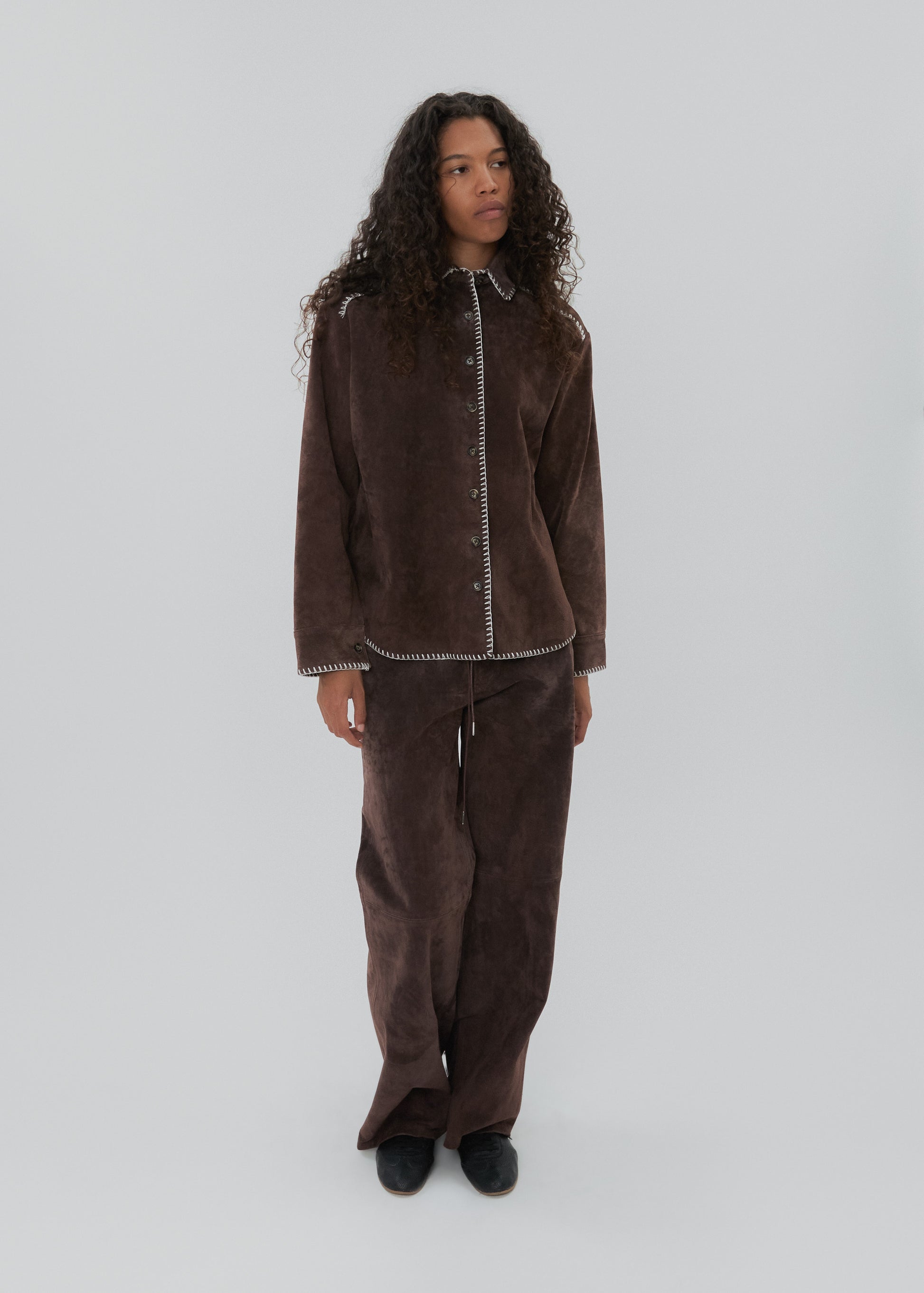 Person wearing a brown outfit with white trim on a light gray background