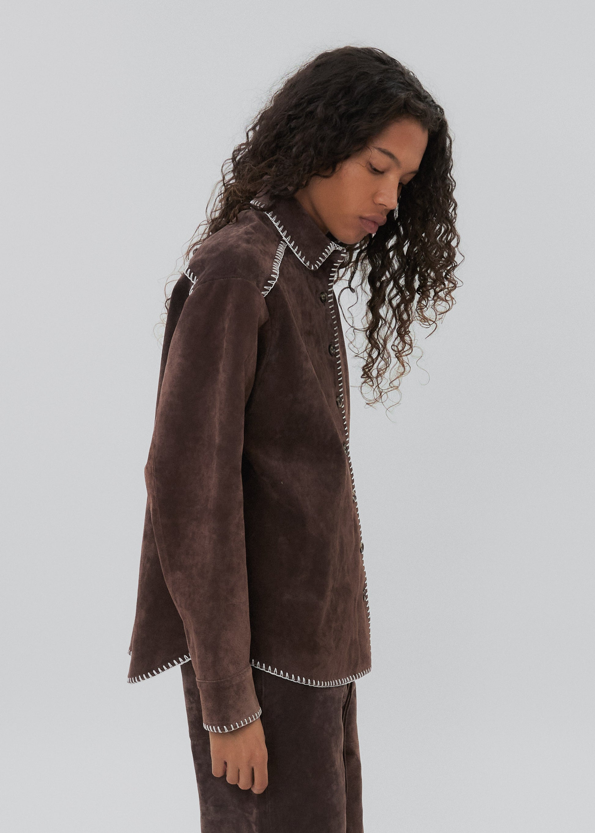 Woman wearing a brown textured jacket and pants on a light gray background