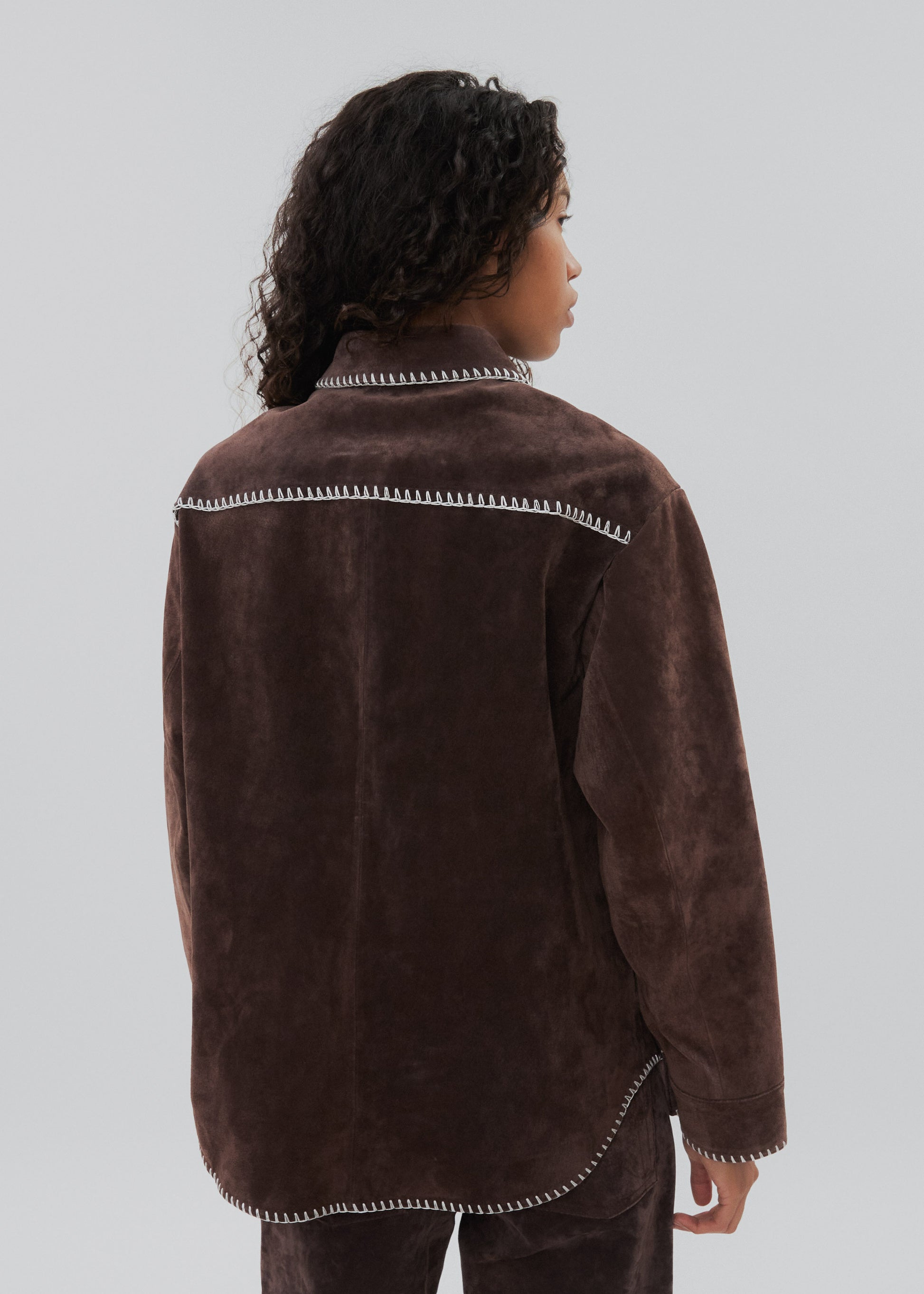 Person wearing a brown jacket with white trim on a plain background