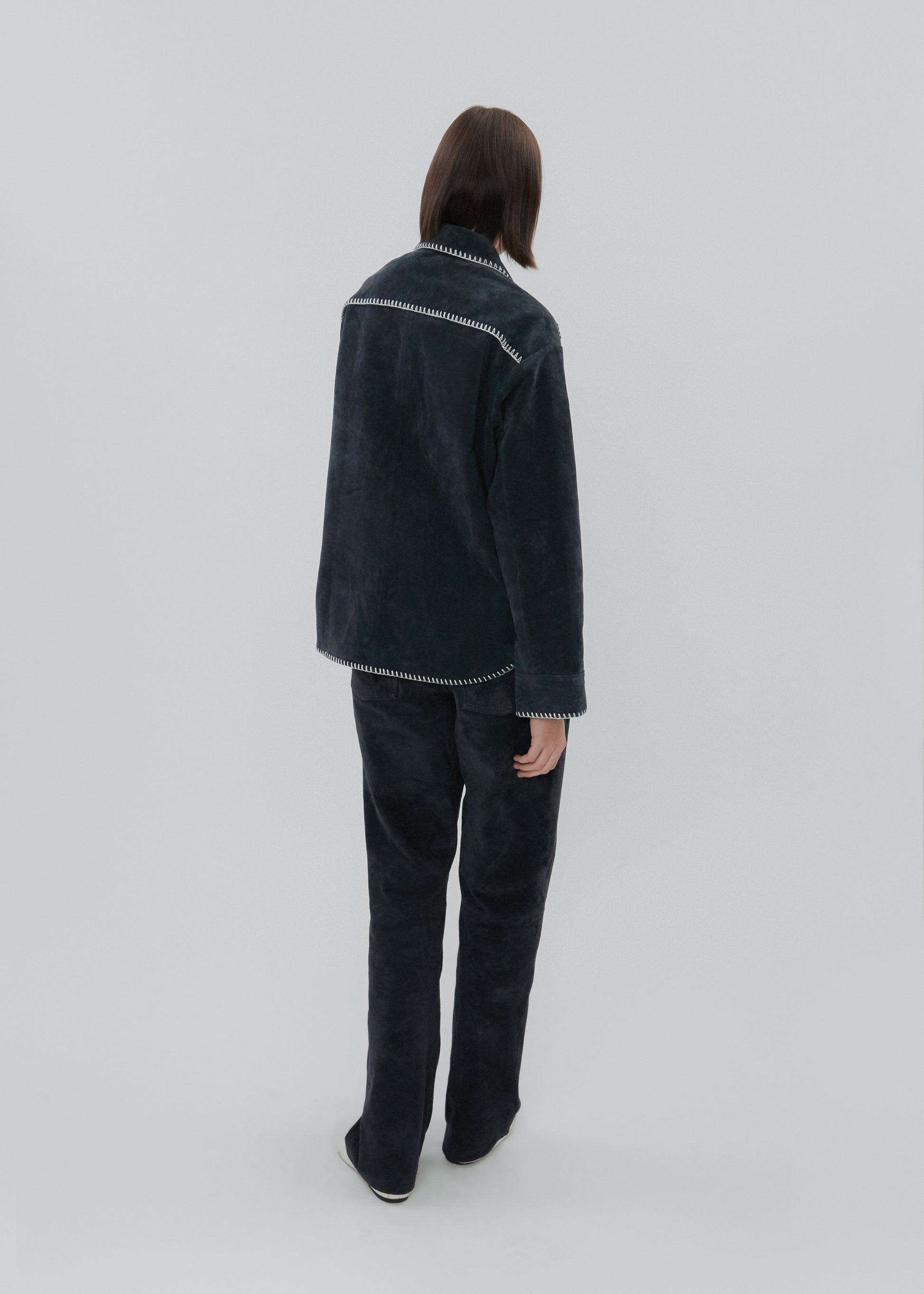 Person wearing a dark denim jacket and pants on a light gray background