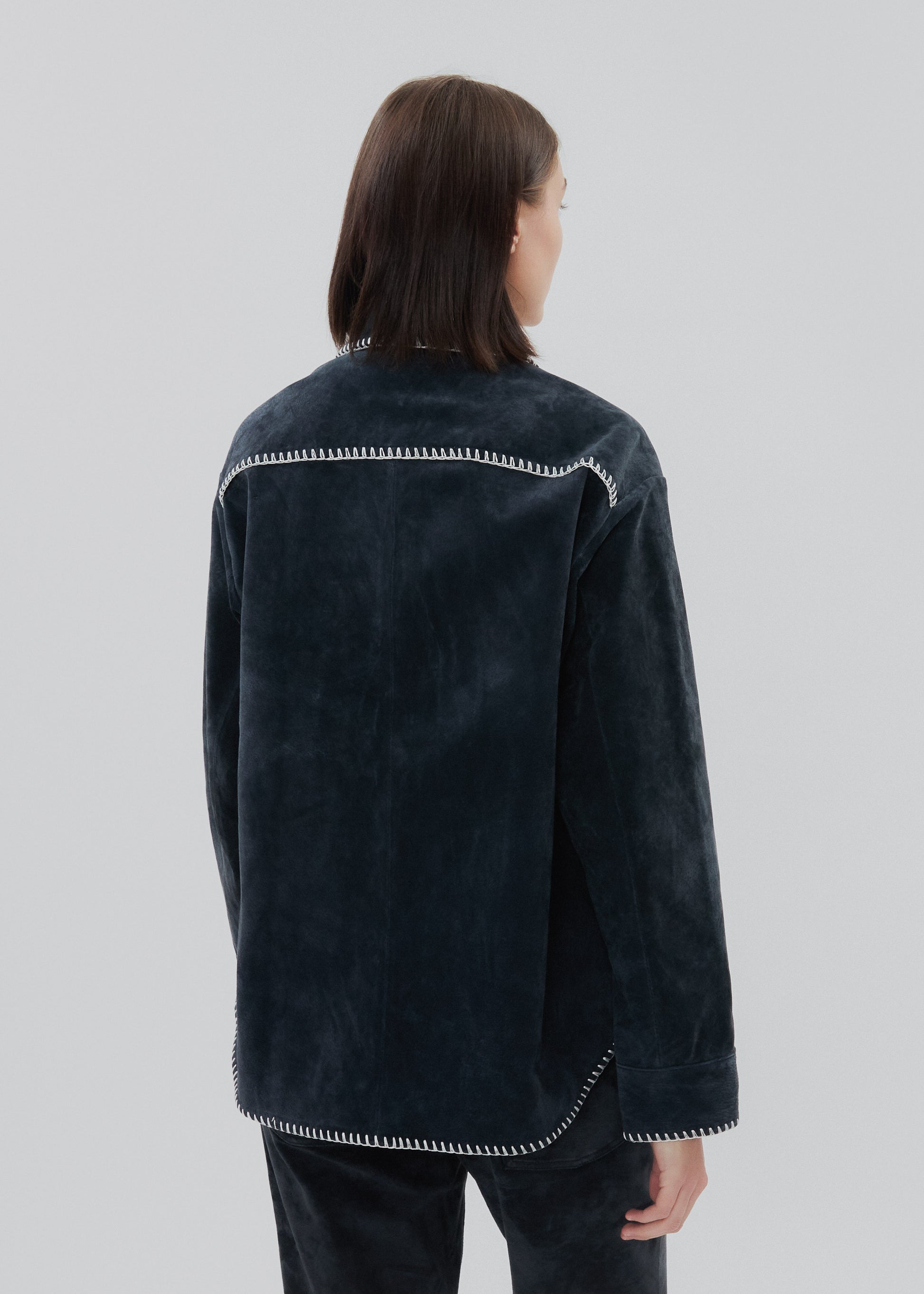 Person wearing a dark denim jacket with white stitching on a light gray background