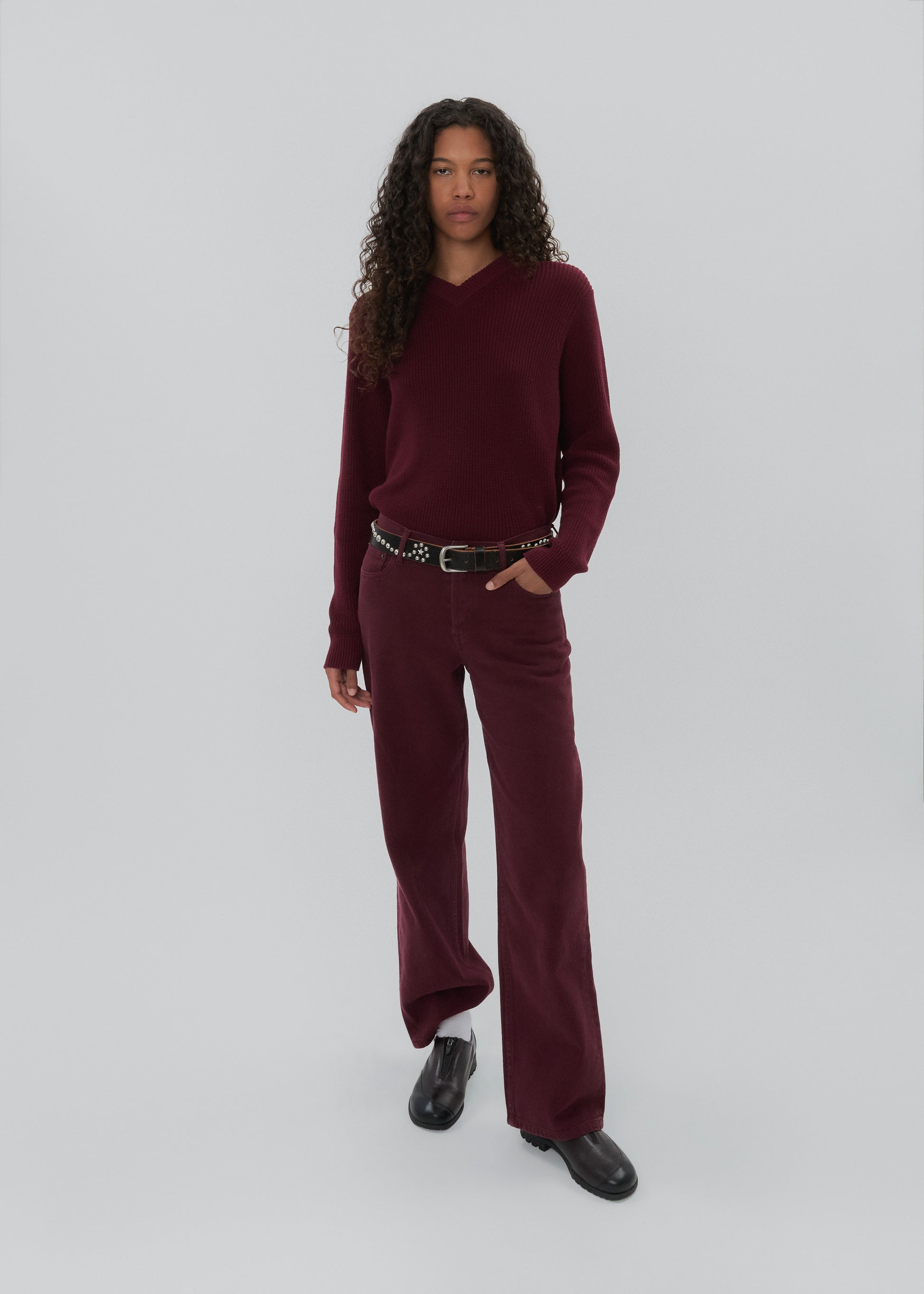 Person wearing a burgundy outfit with a belt on a white background