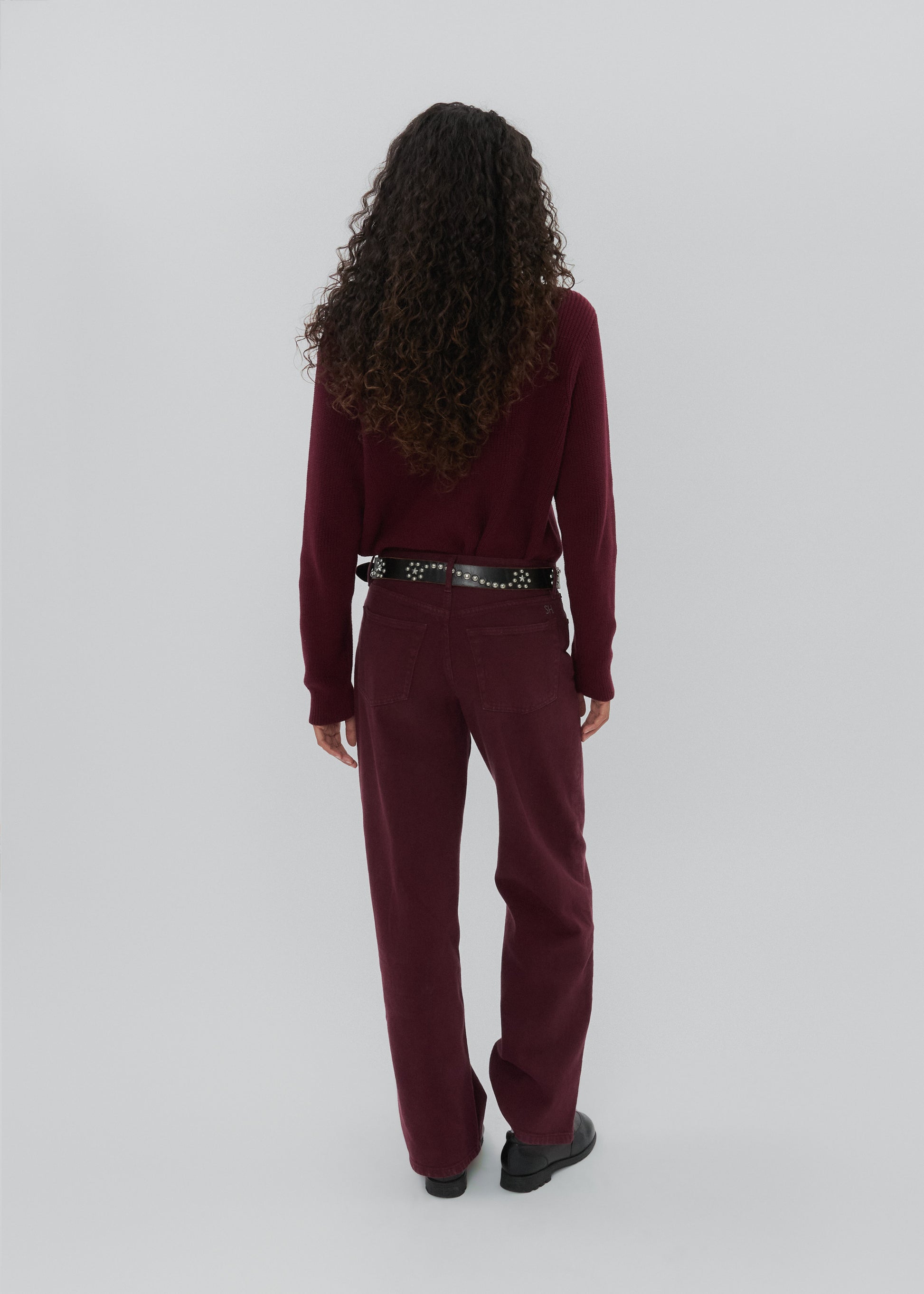Person wearing a burgundy outfit with a belt on a white background