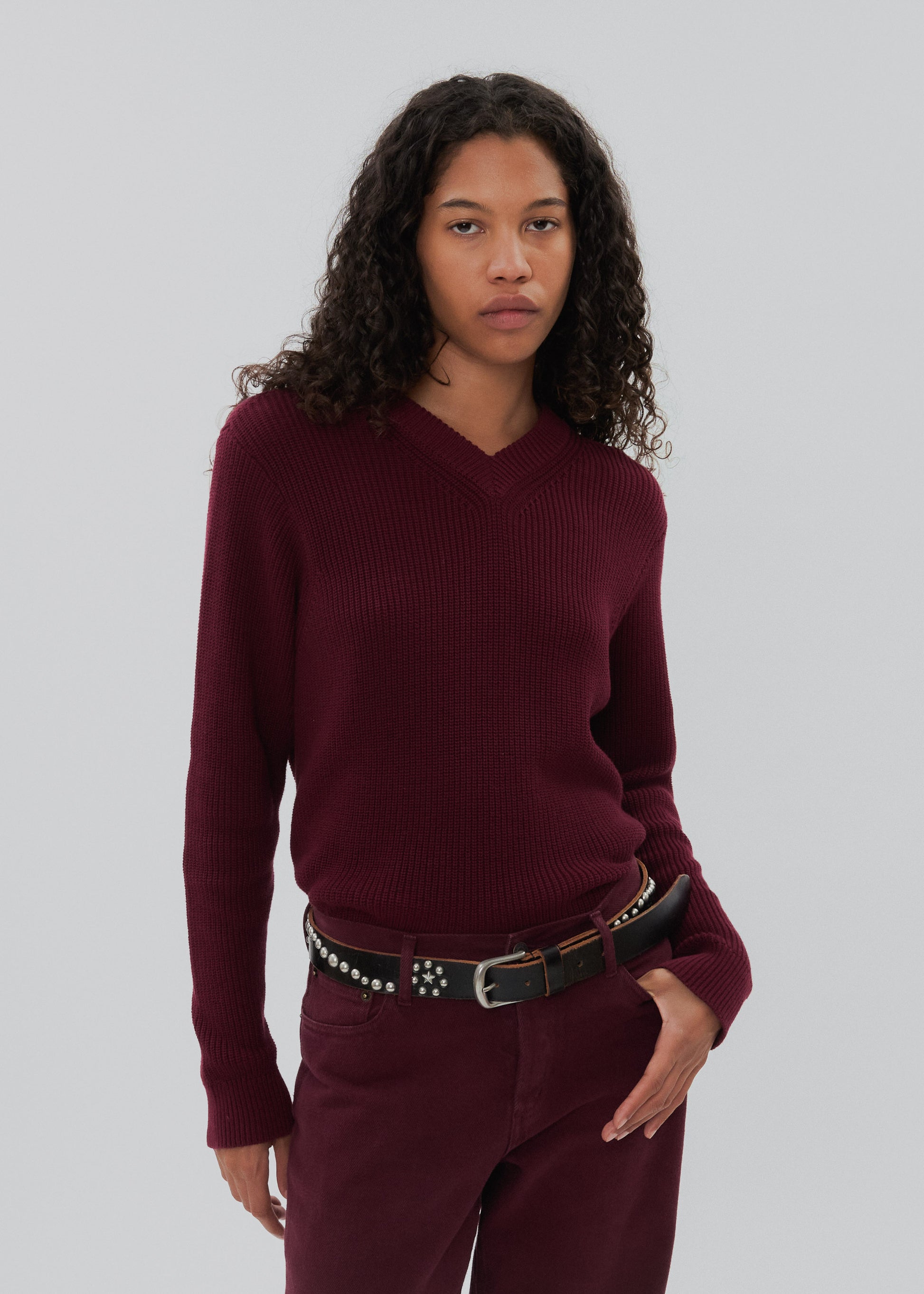 Woman wearing a burgundy sweater and pants against a plain background