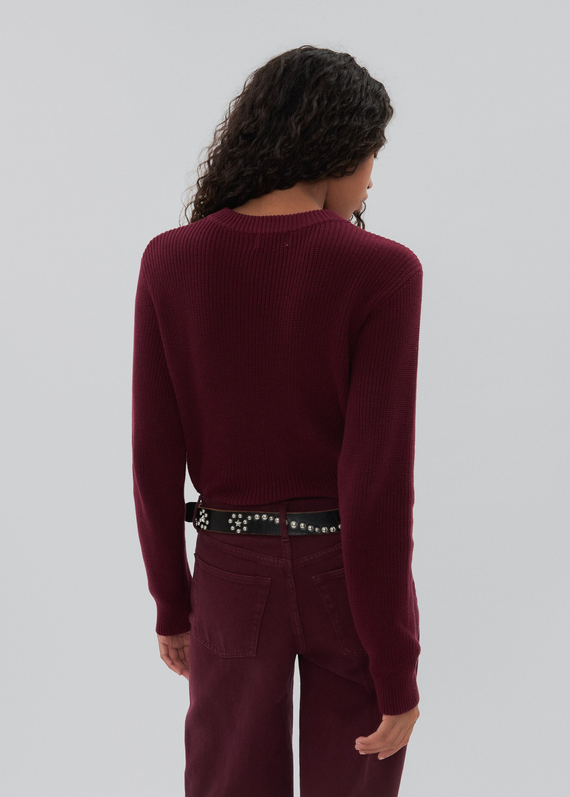 Person wearing a burgundy sweater and pants with a plain background