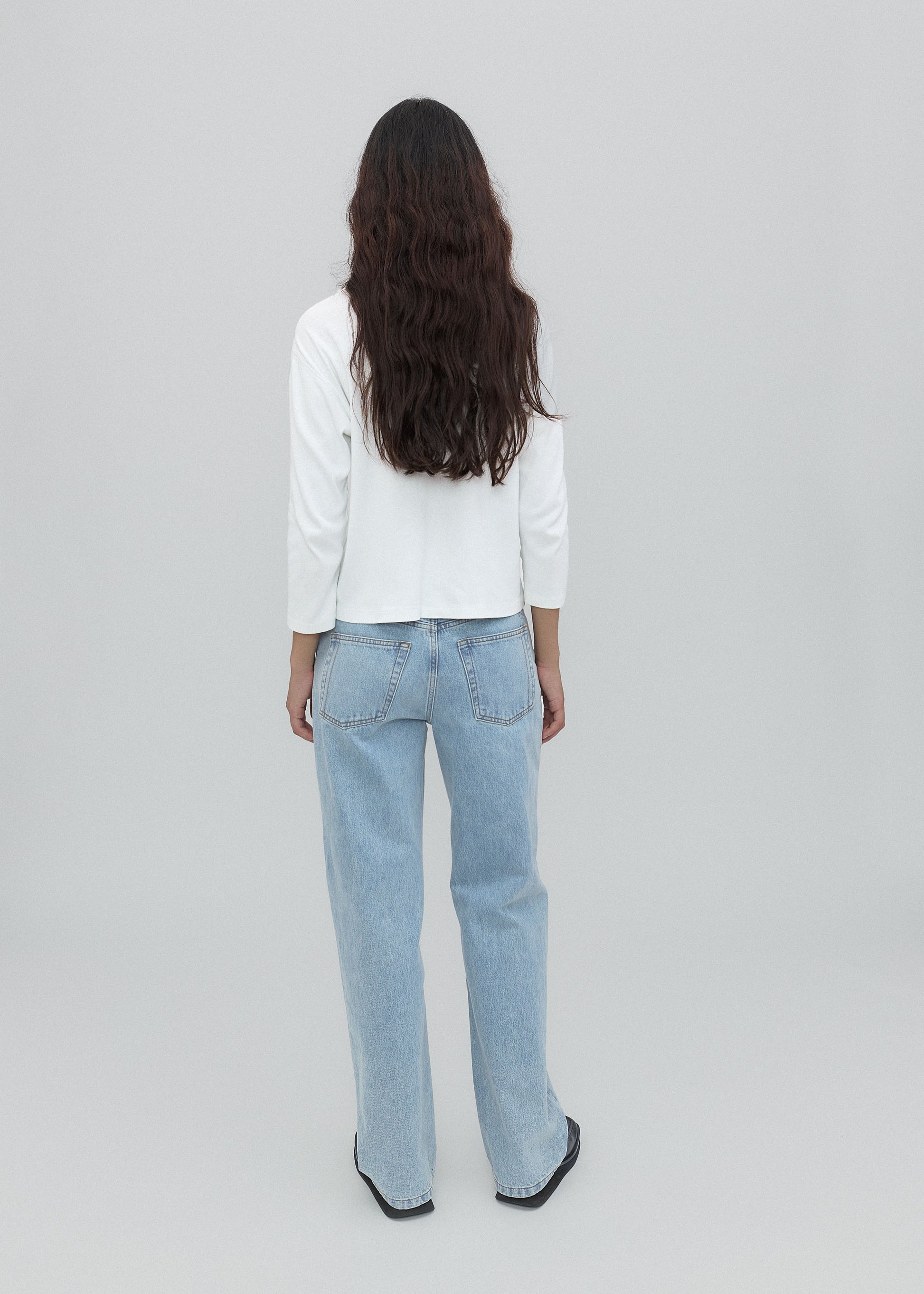 Person wearing light blue jeans and a white shirt on a plain background