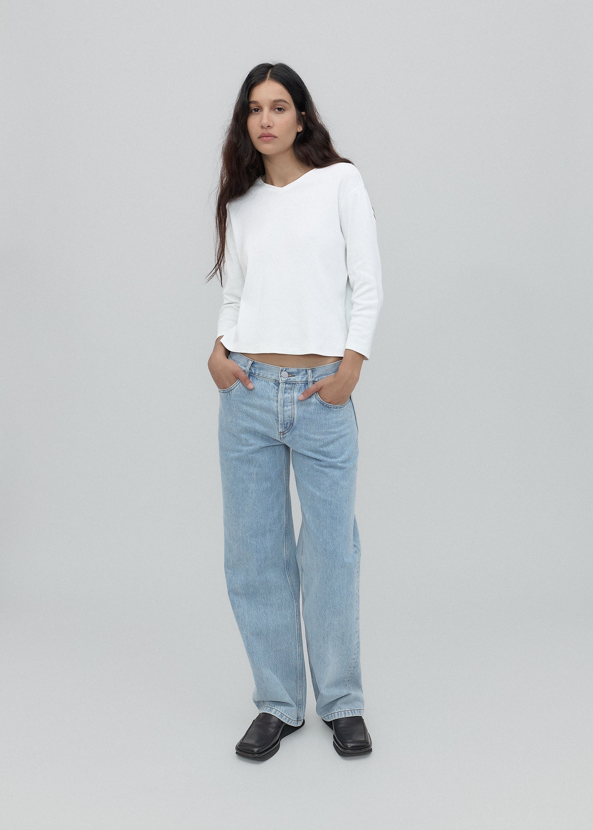 Woman wearing a white sweater and light blue jeans on a gray background