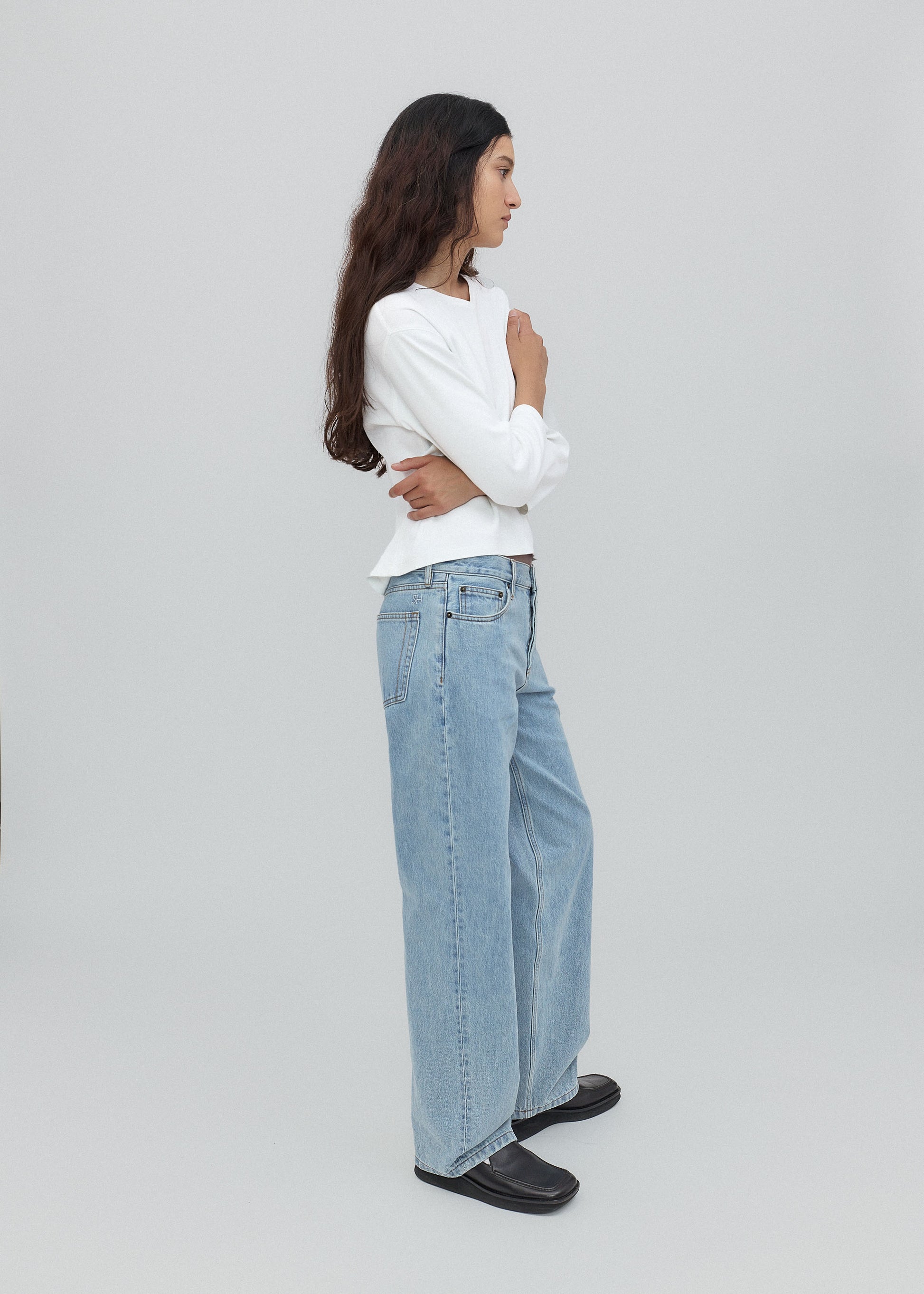 Woman wearing a white sweater and light blue jeans on a plain background