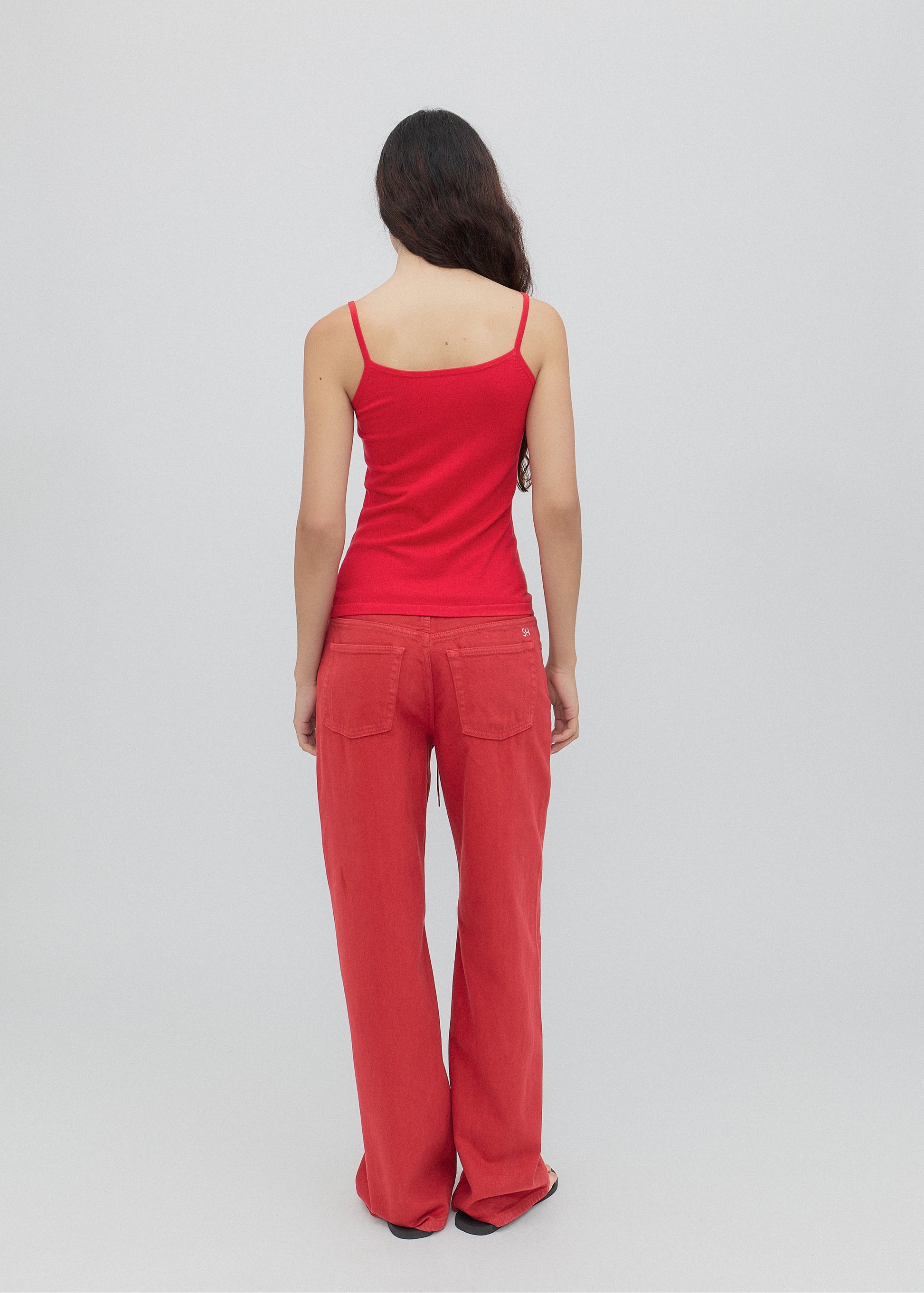 Person wearing a red tank top and pants on a light gray background