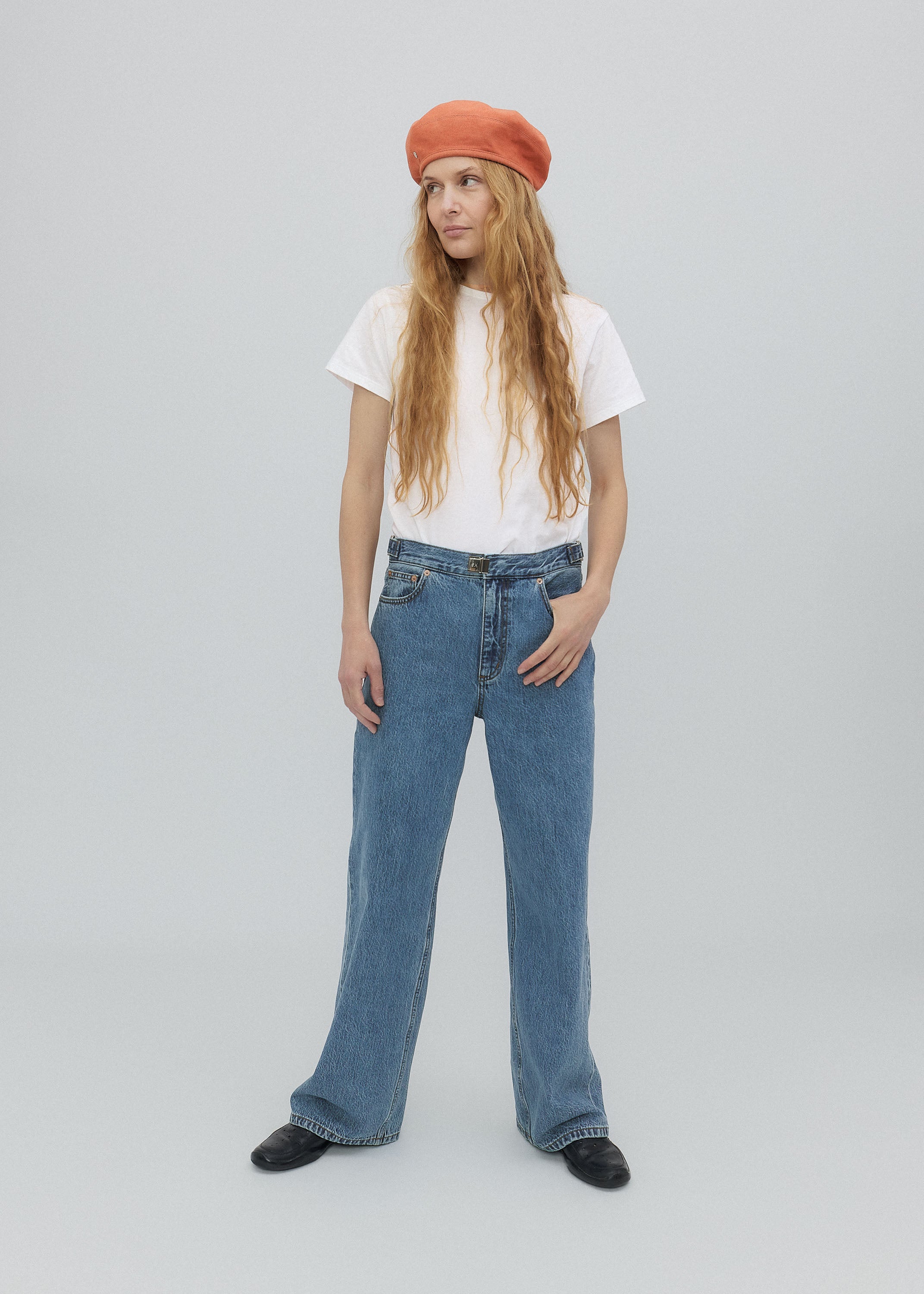 Person wearing a white t-shirt, blue jeans, and an orange beret on a light gray background