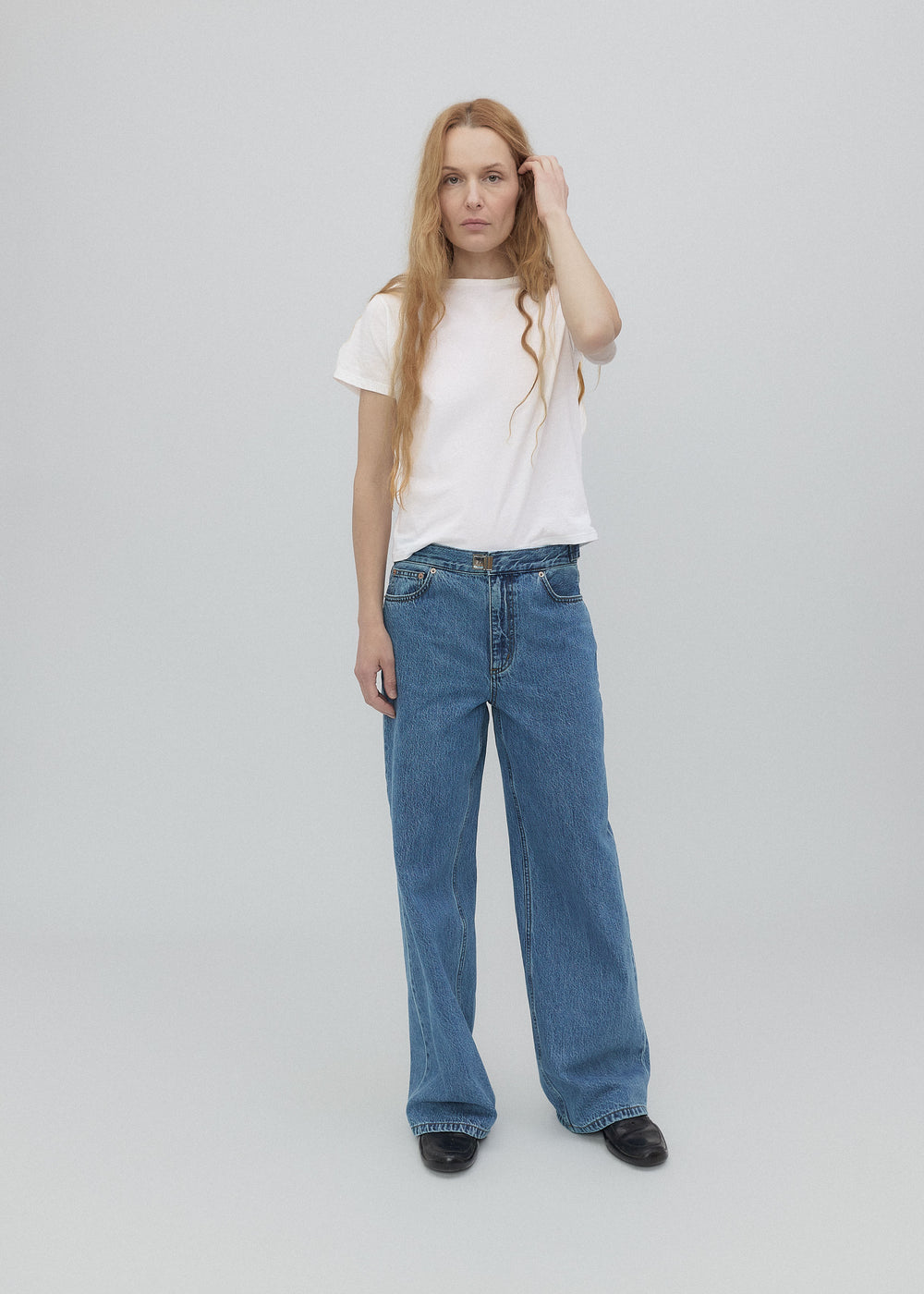 Woman wearing a white t-shirt and blue jeans on a plain background