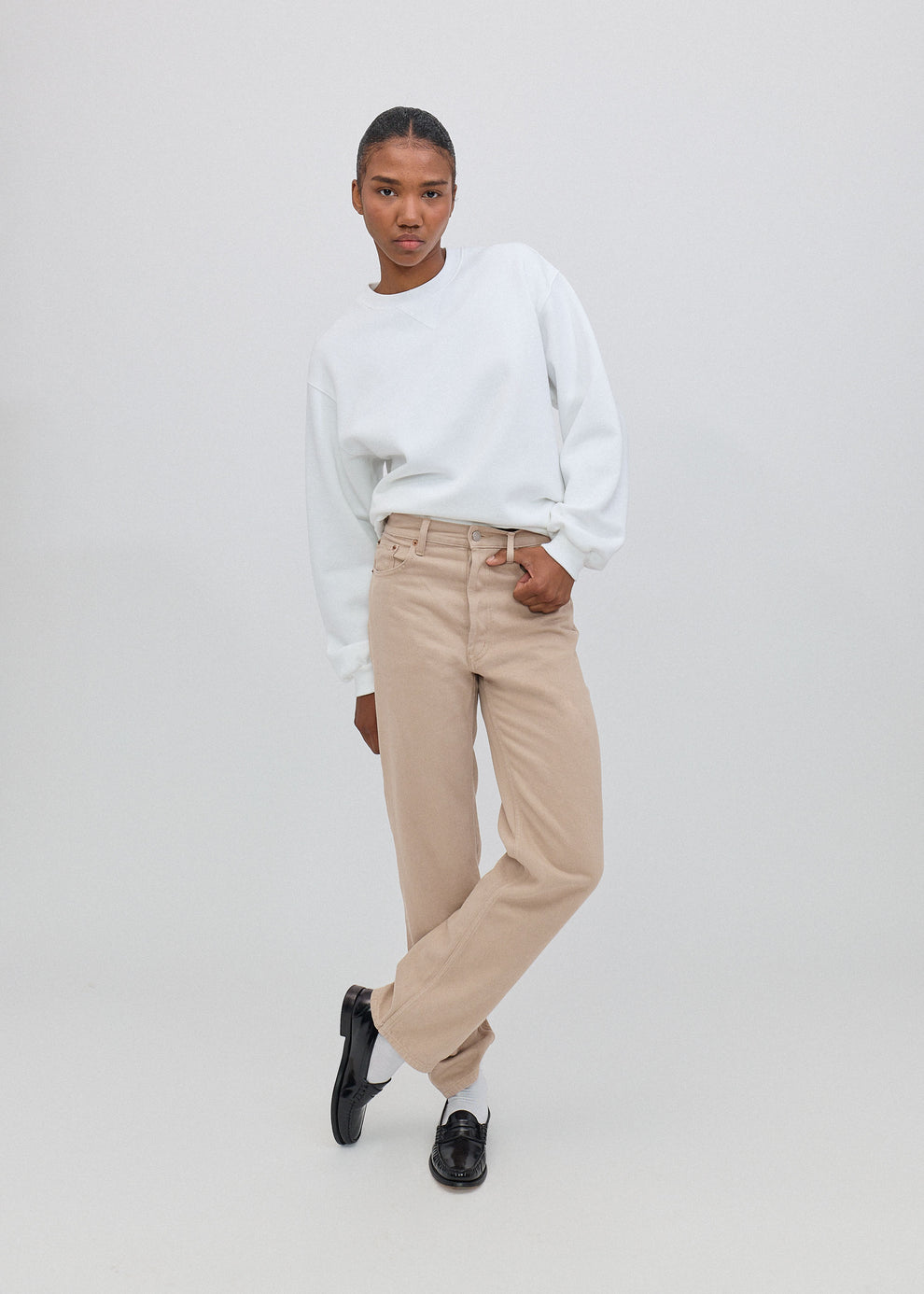 Person wearing a white sweater and beige pants on a plain background