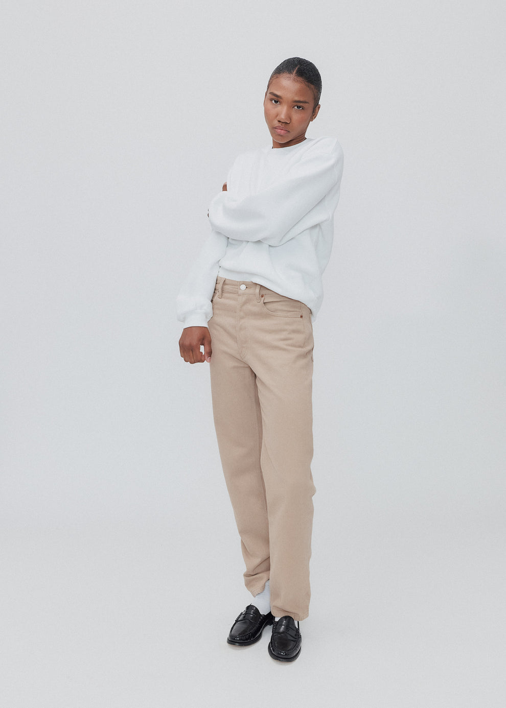 Person wearing a light gray sweater, beige pants, and black shoes on a white background