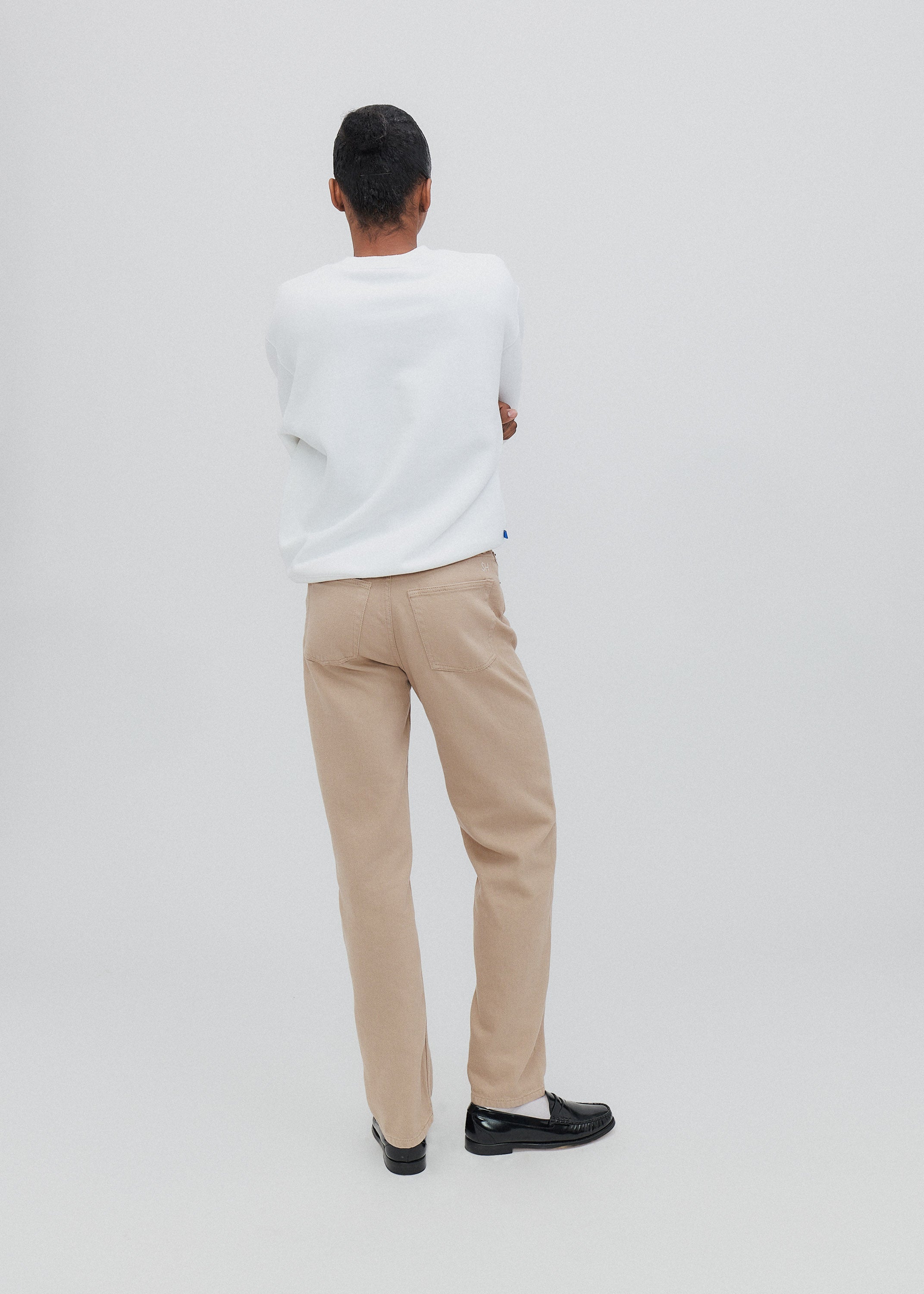 Person wearing a white shirt and beige pants on a plain background