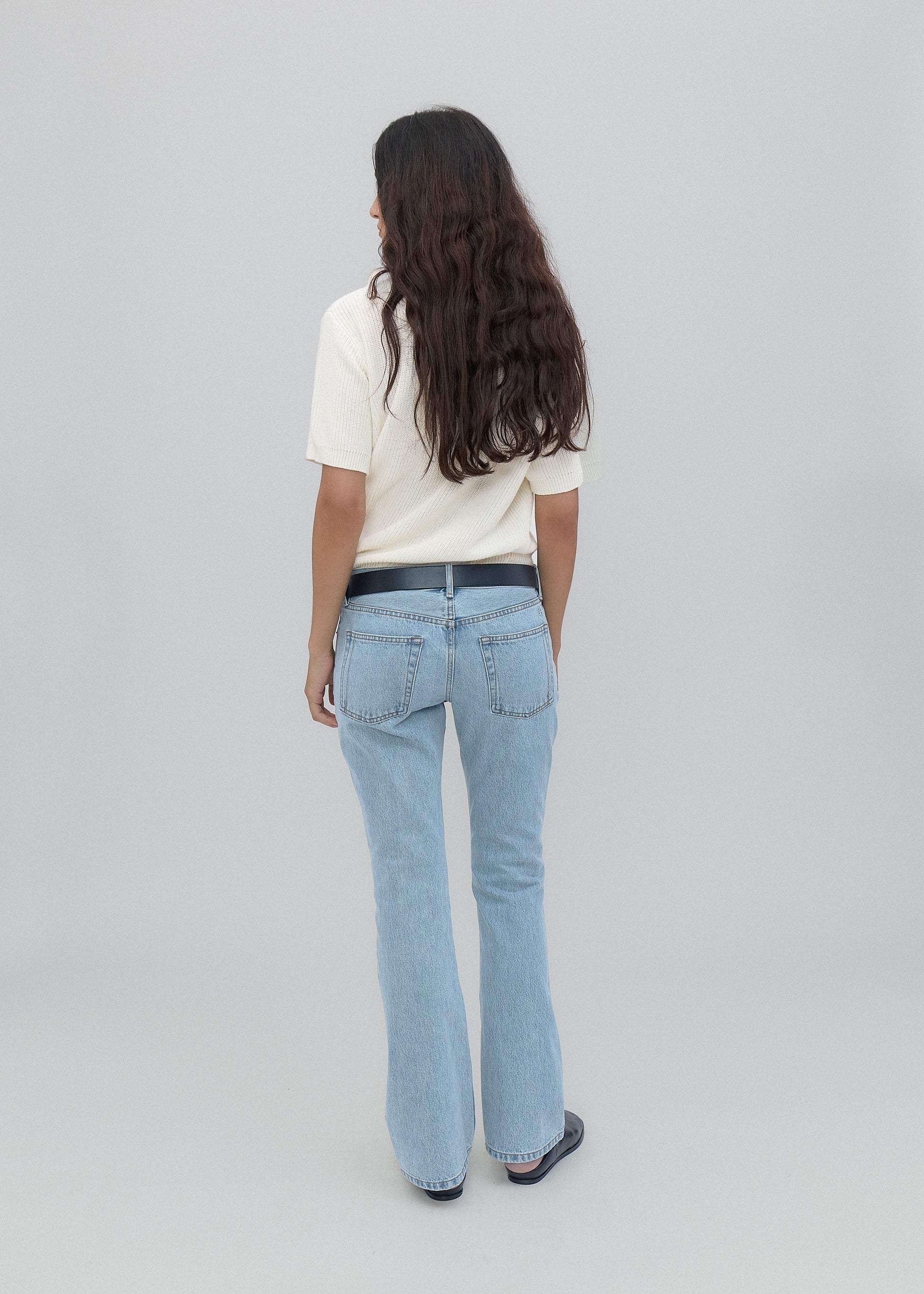 Person wearing light blue jeans and a white shirt on a plain background