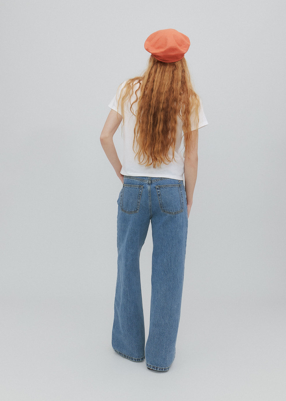 Person wearing a white shirt, blue jeans, and an orange beret on a plain background