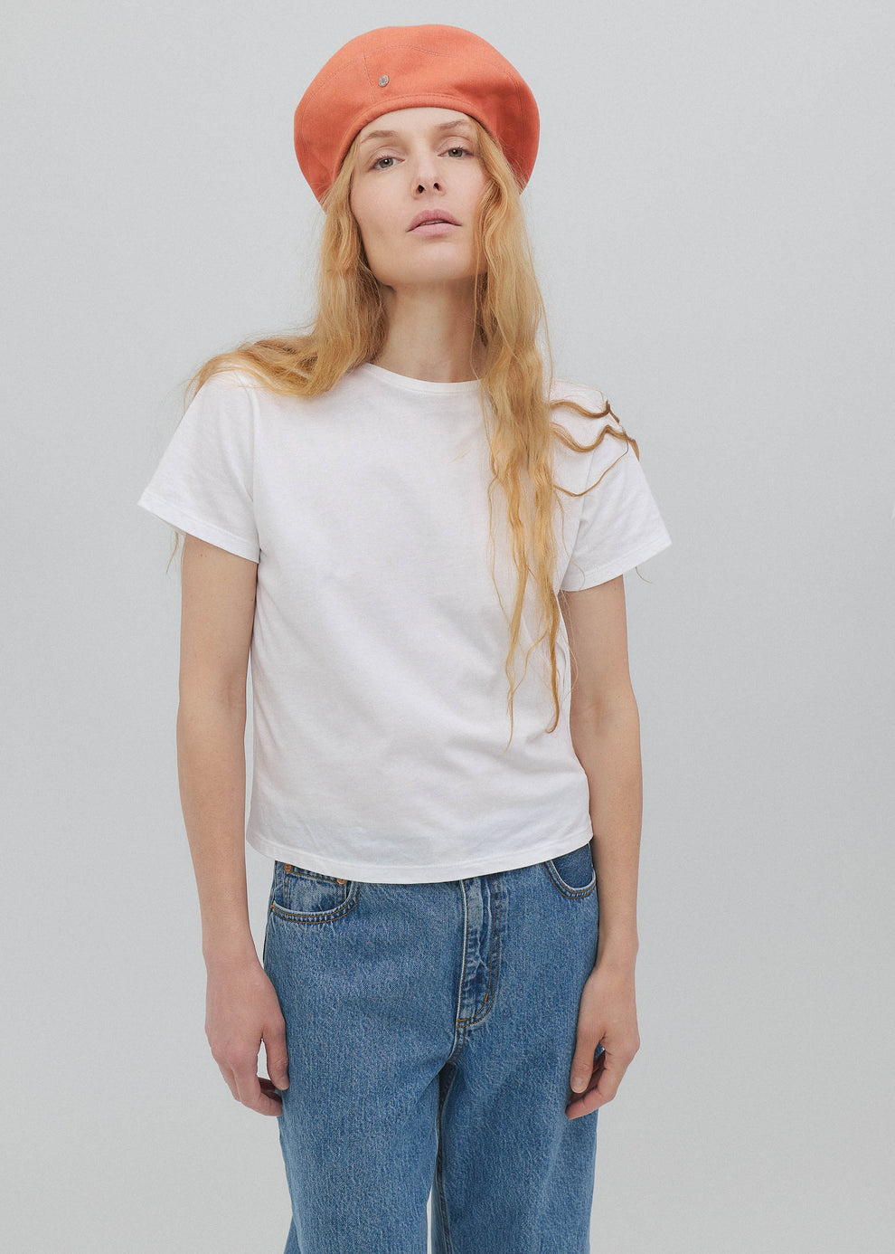Person wearing a white t-shirt, blue jeans, and an orange beret on a plain background